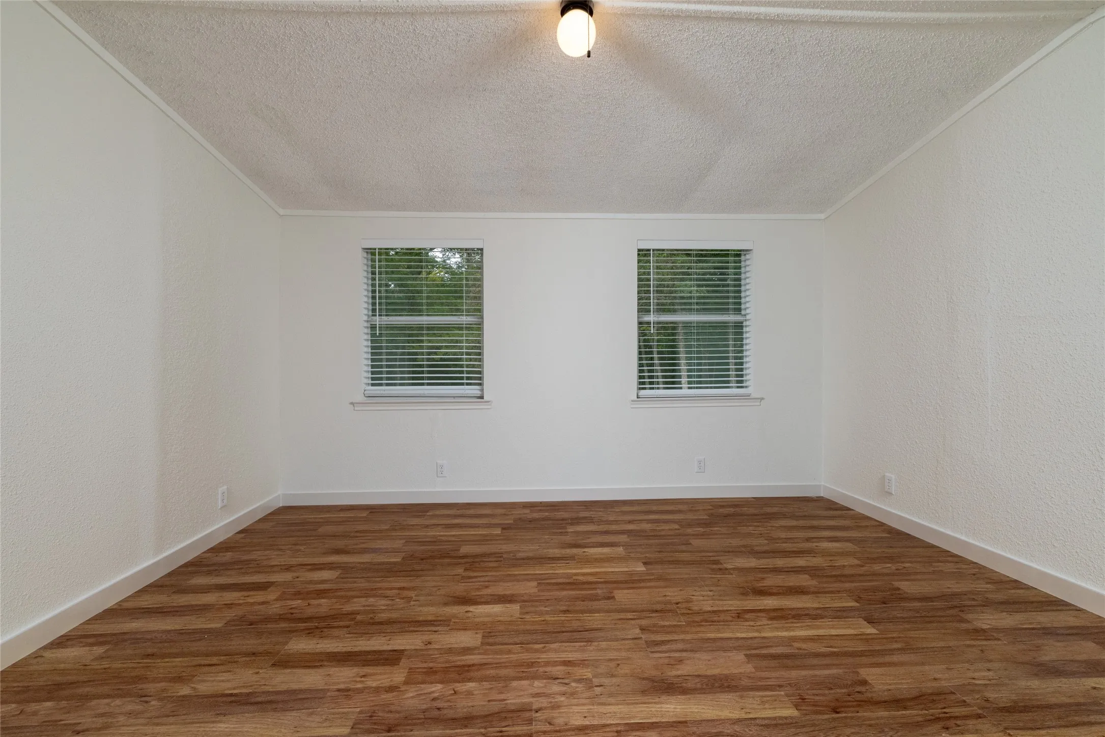 Room featuring wood-finish flooring, white walls, and two windows with horizontal blinds