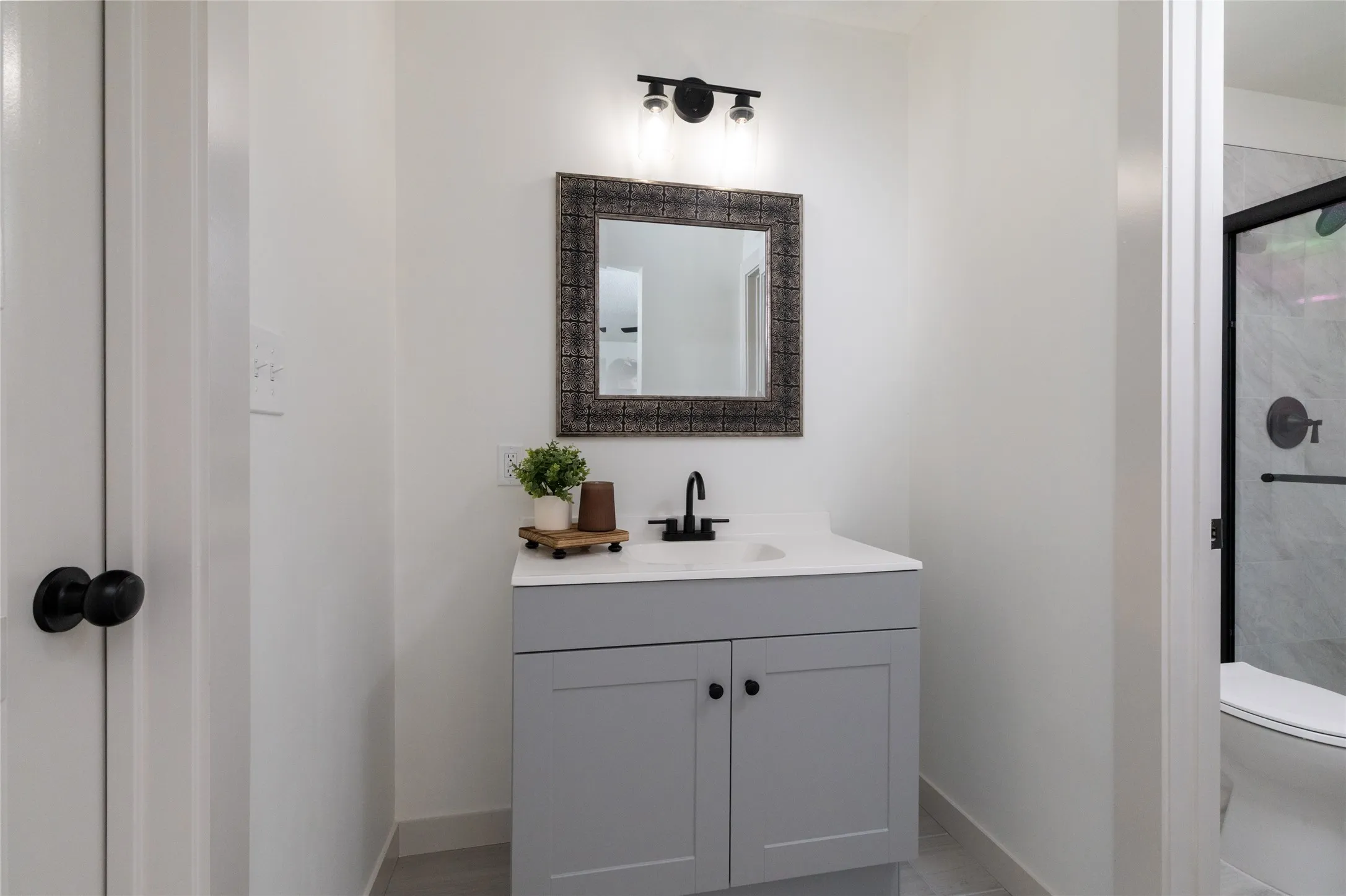 Modern bathroom vanity featuring a light gray cabinet, white countertop, and black hardware
