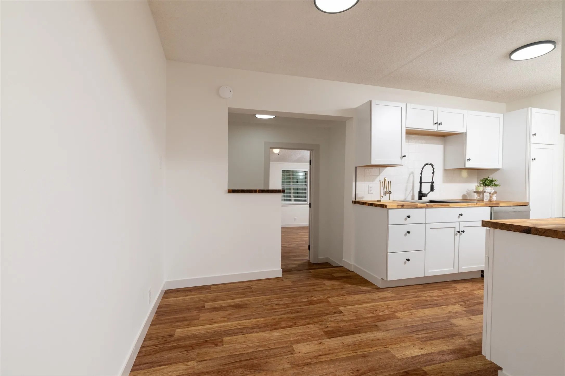 Kitchen featuring white cabinetry, wood-finish countertops, black sink and faucet, and subway tile backsplash