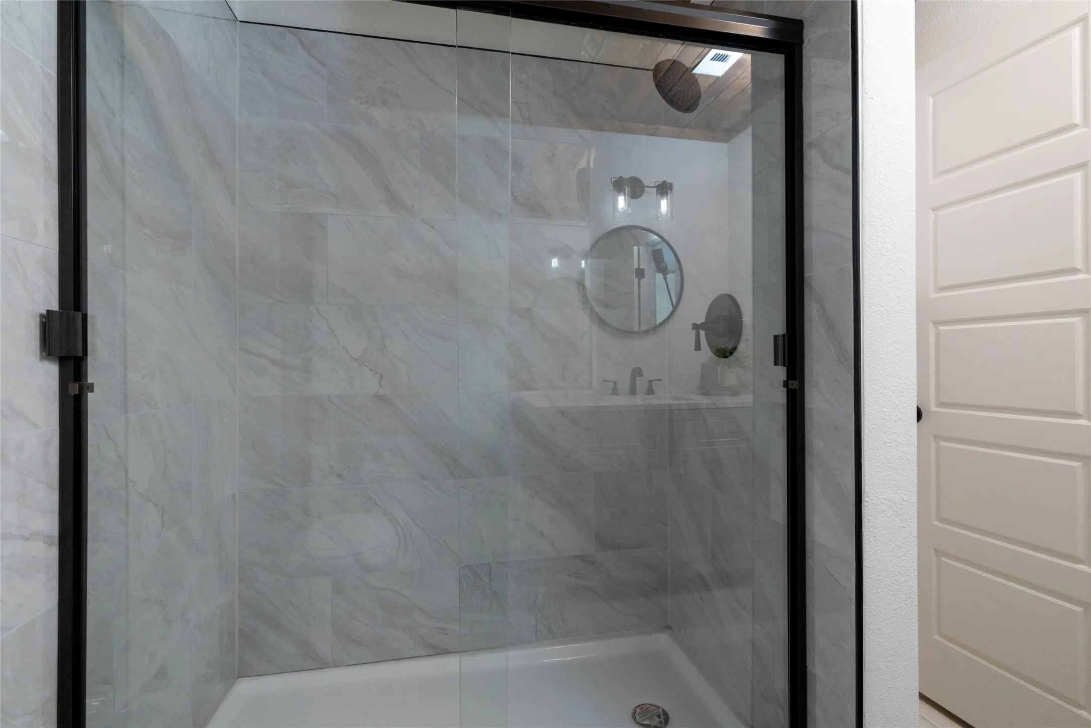 Glass-enclosed shower featuring large format light gray wall tile, a built-in shower niche, and a contrasting dark-finished shower head