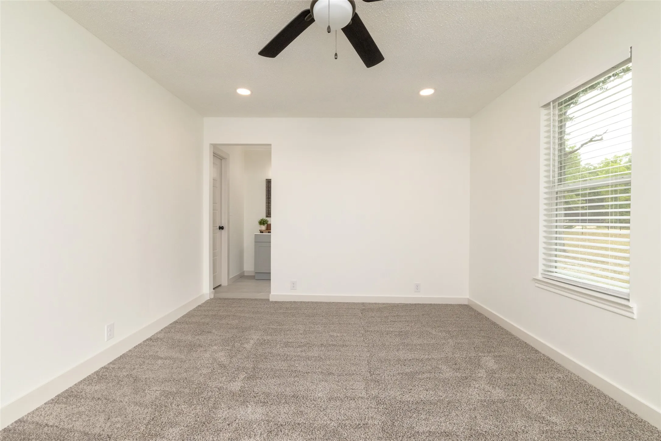 Spacious room featuring neutral carpeting, white walls, a ceiling fan with light, recessed lighting, and a window with blinds