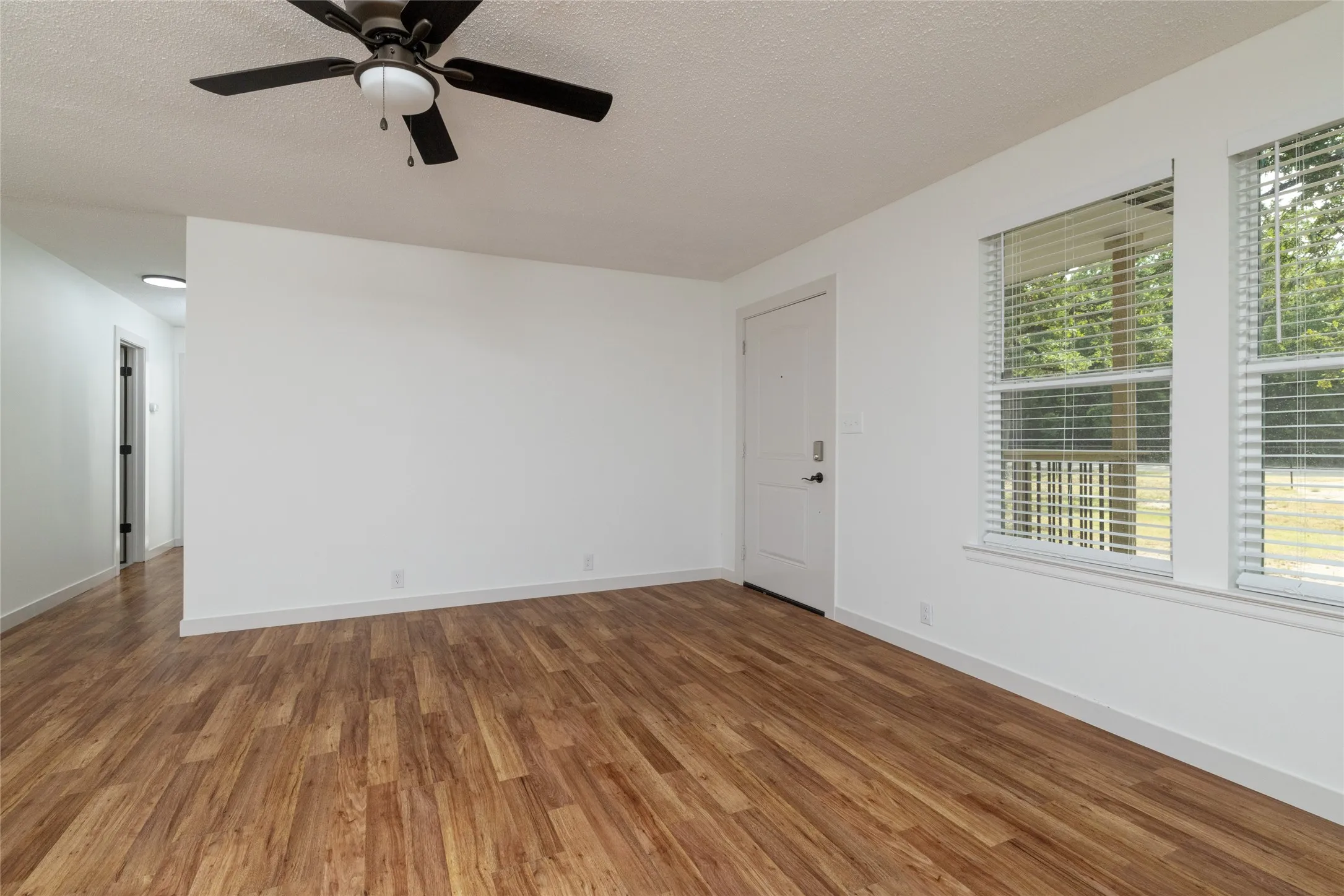 Living area featuring wood-finish flooring, white walls, and a ceiling fan with integrated lighting
