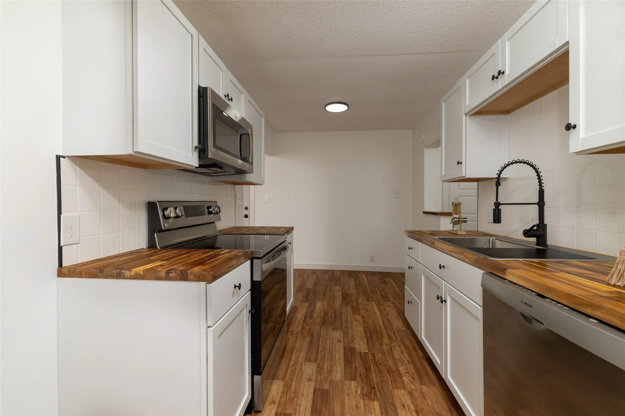Modern kitchen featuring white shaker cabinetry, wood-finish countertops, stainless steel appliances, and wood-finish flooring