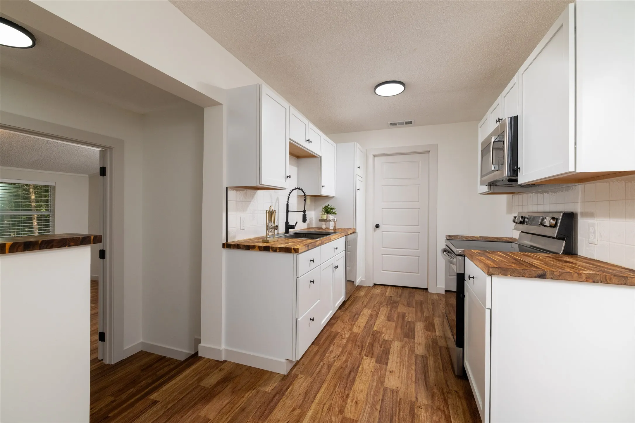 Modern kitchen featuring white shaker-style cabinetry, wood-finish countertops, subway tile backsplash, and wood-finish flooring