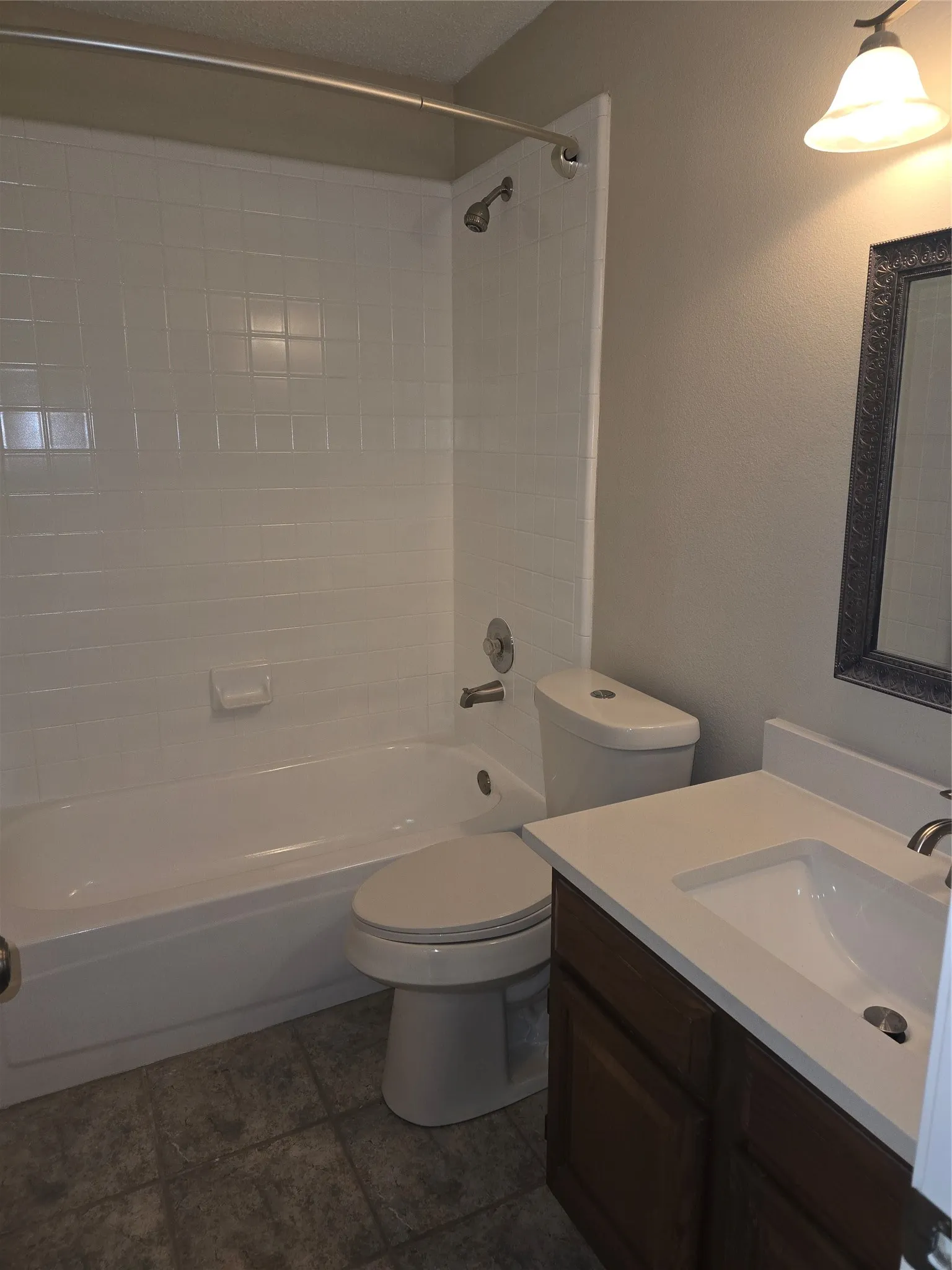 Full bathroom featuring a white tub/shower combination with subway-style wall tiling, a white toilet, and a dark wood-finish vanity with an integrated white sink and counter