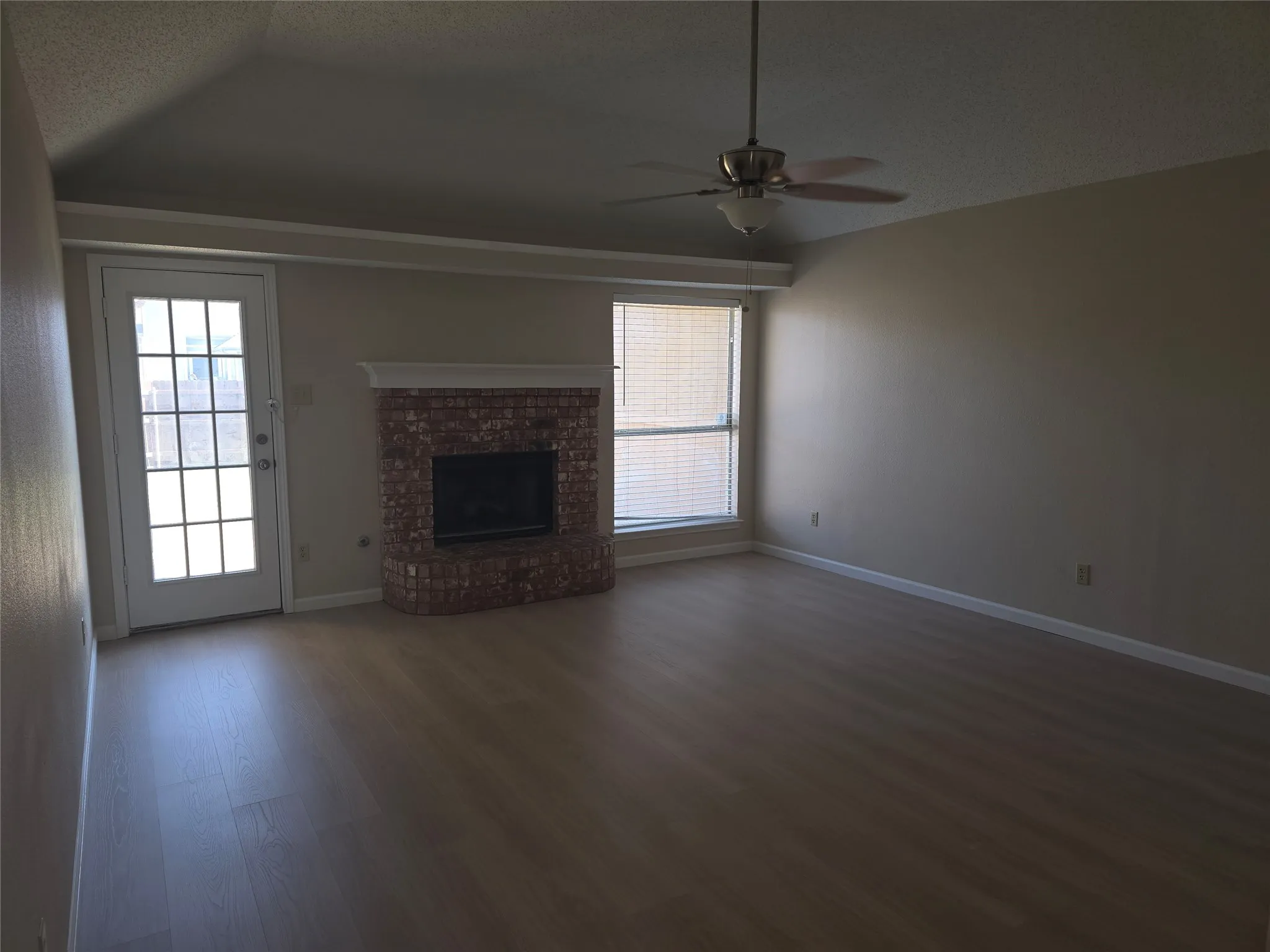 Living area featuring wood-finish flooring, a brick fireplace with a white mantel, and a ceiling fan