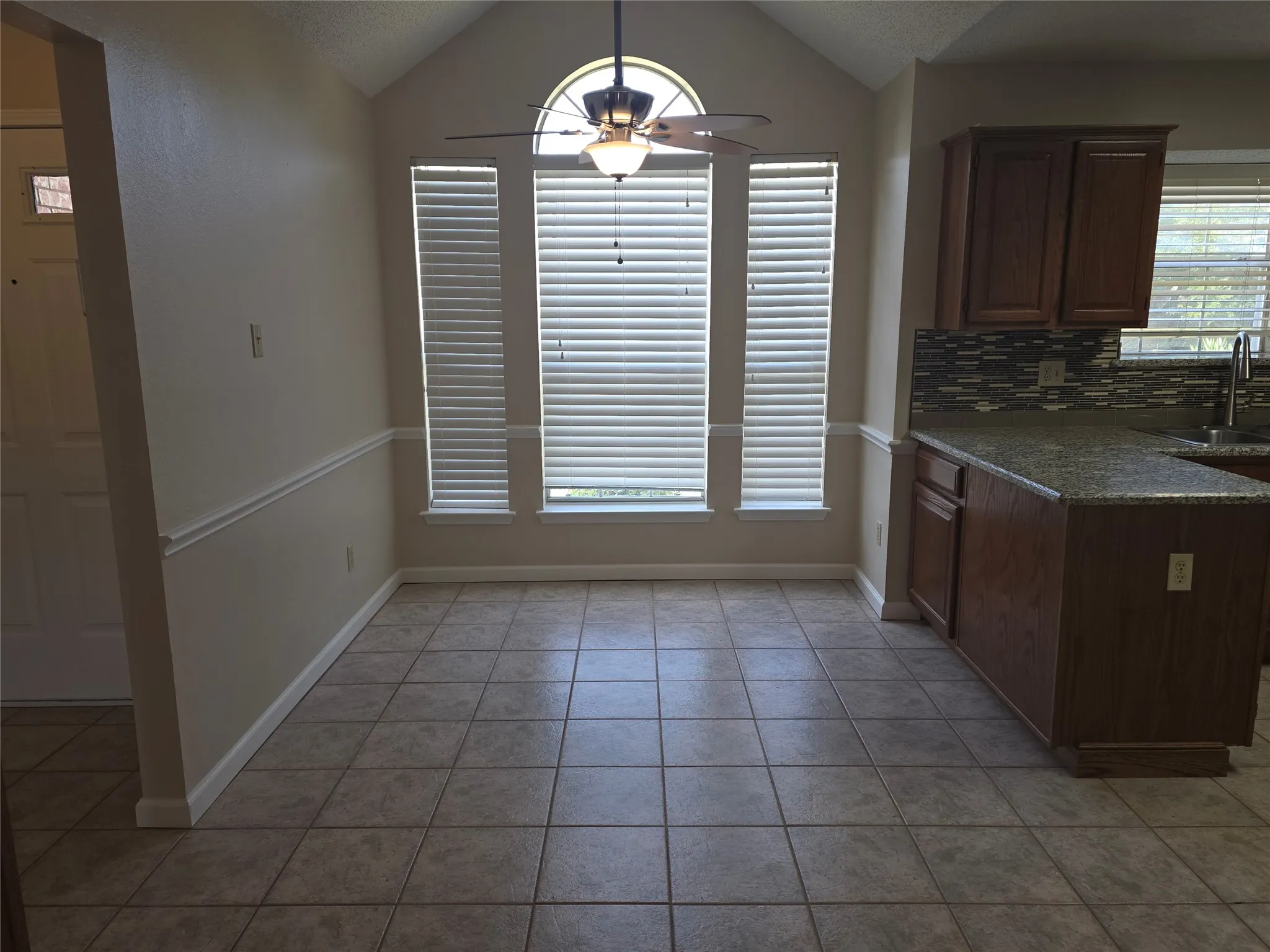 Kitchen dining area featuring vaulted ceilings, three vertical windows with blinds, and a semi-flush mount ceiling fan