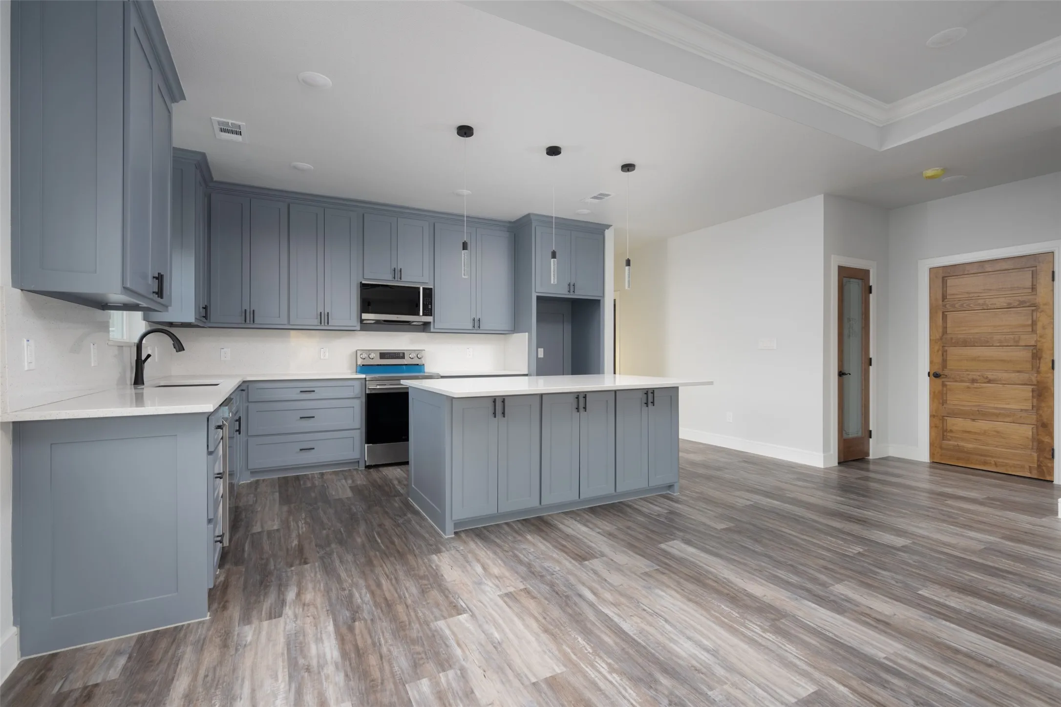 Open-concept kitchen featuring blue shaker-style cabinetry, white countertops, and wood-finish flooring