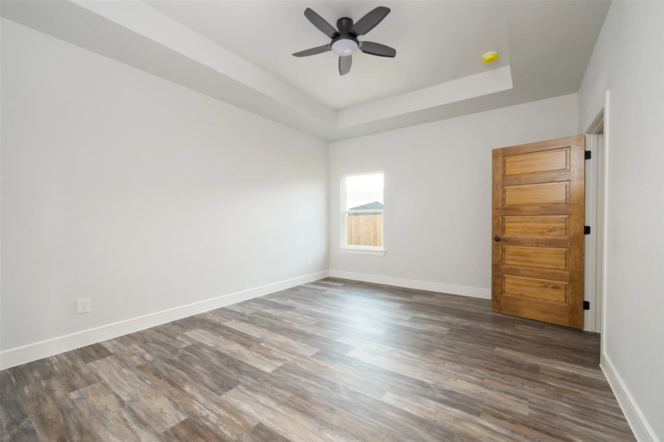 Spacious interior room featuring wood-finish flooring, a tray ceiling, and a modern ceiling fan