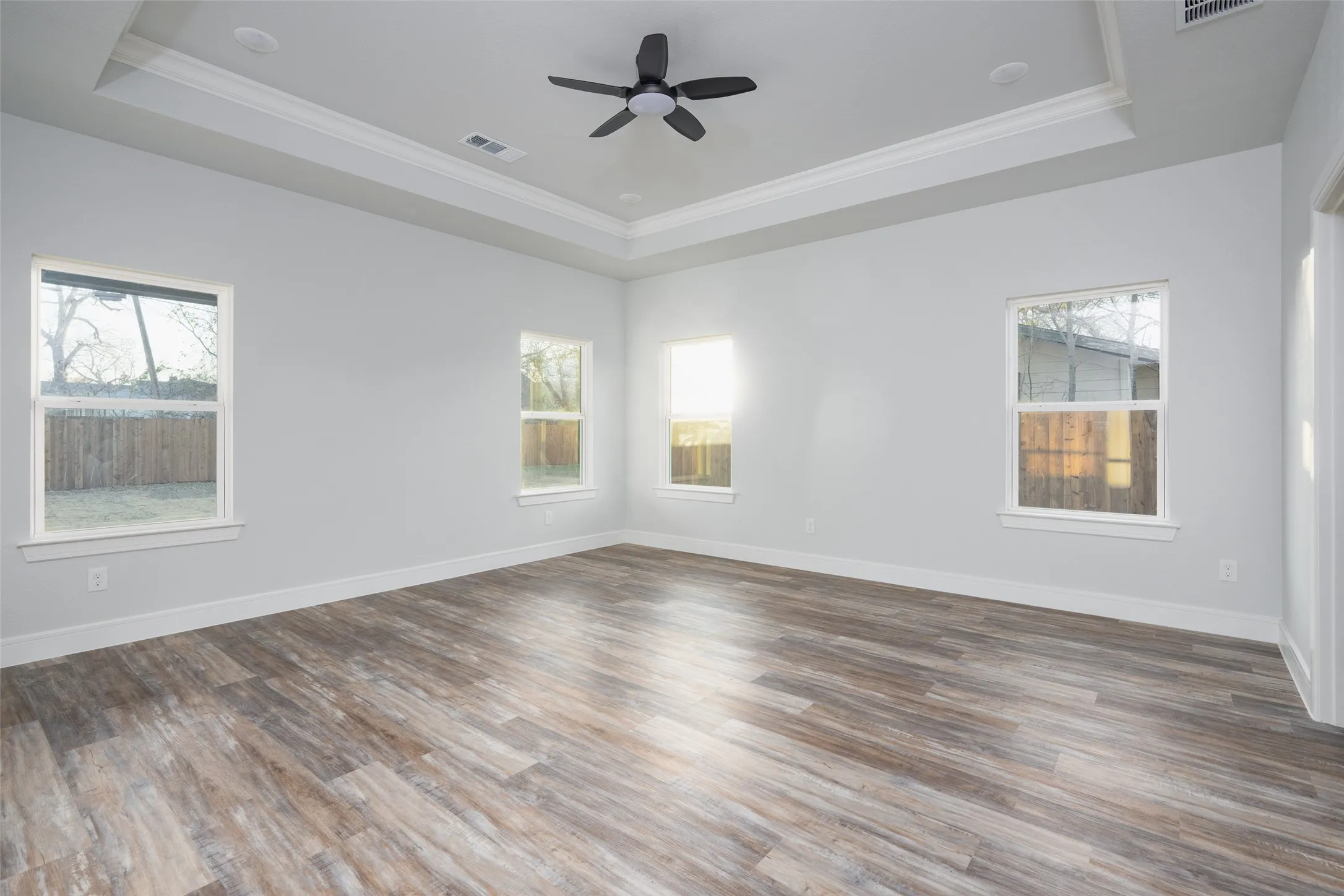 Spacious room featuring wood-finish flooring, a tray ceiling with crown molding, and a ceiling fan