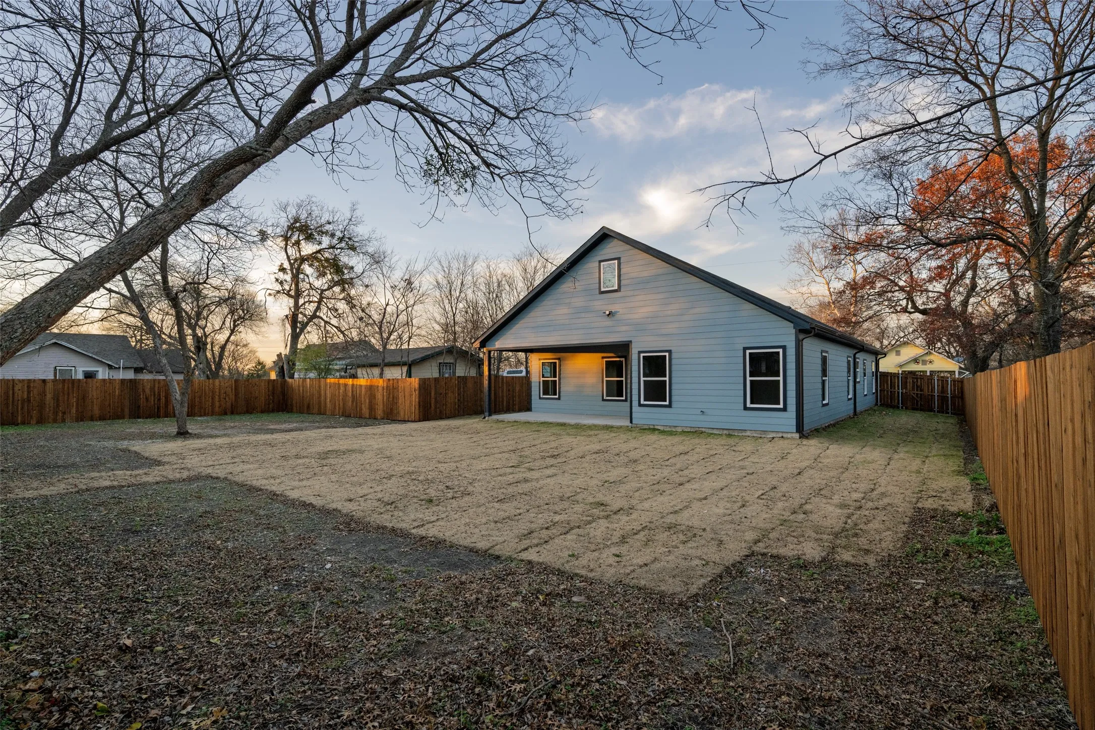 Spacious backyard featuring a newly installed privacy fence, light blue siding exterior, black trim windows, and a covered patio area