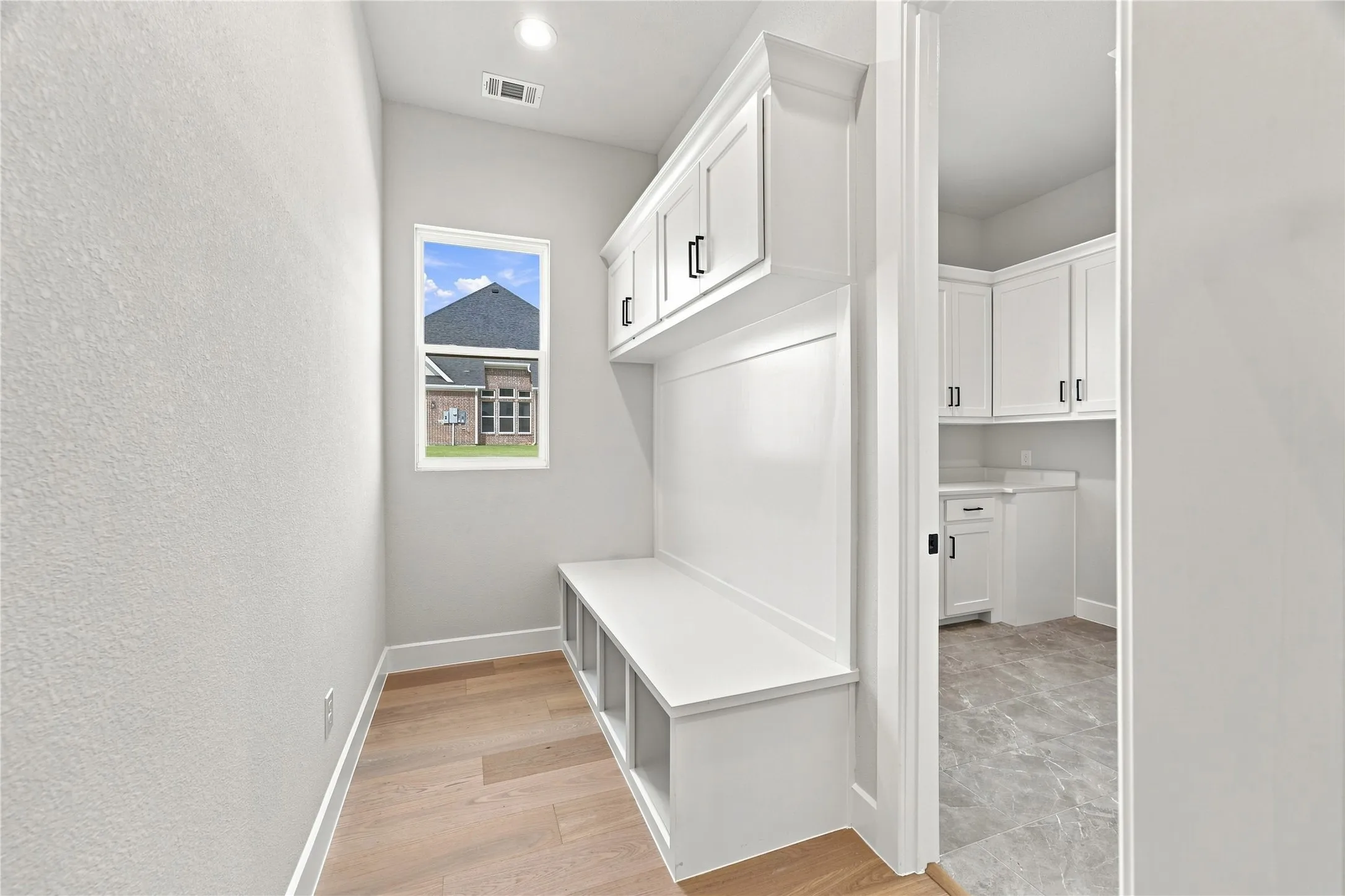 Built-in bench with cubby storage, upper cabinetry with black hardware, and wood-finish flooring