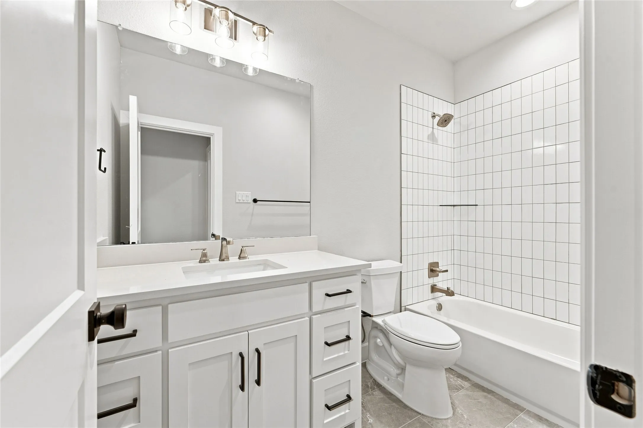 White vanity with integrated sink and brushed nickel faucet, large mirror, vertical subway tile shower surround, and grey tile flooring
