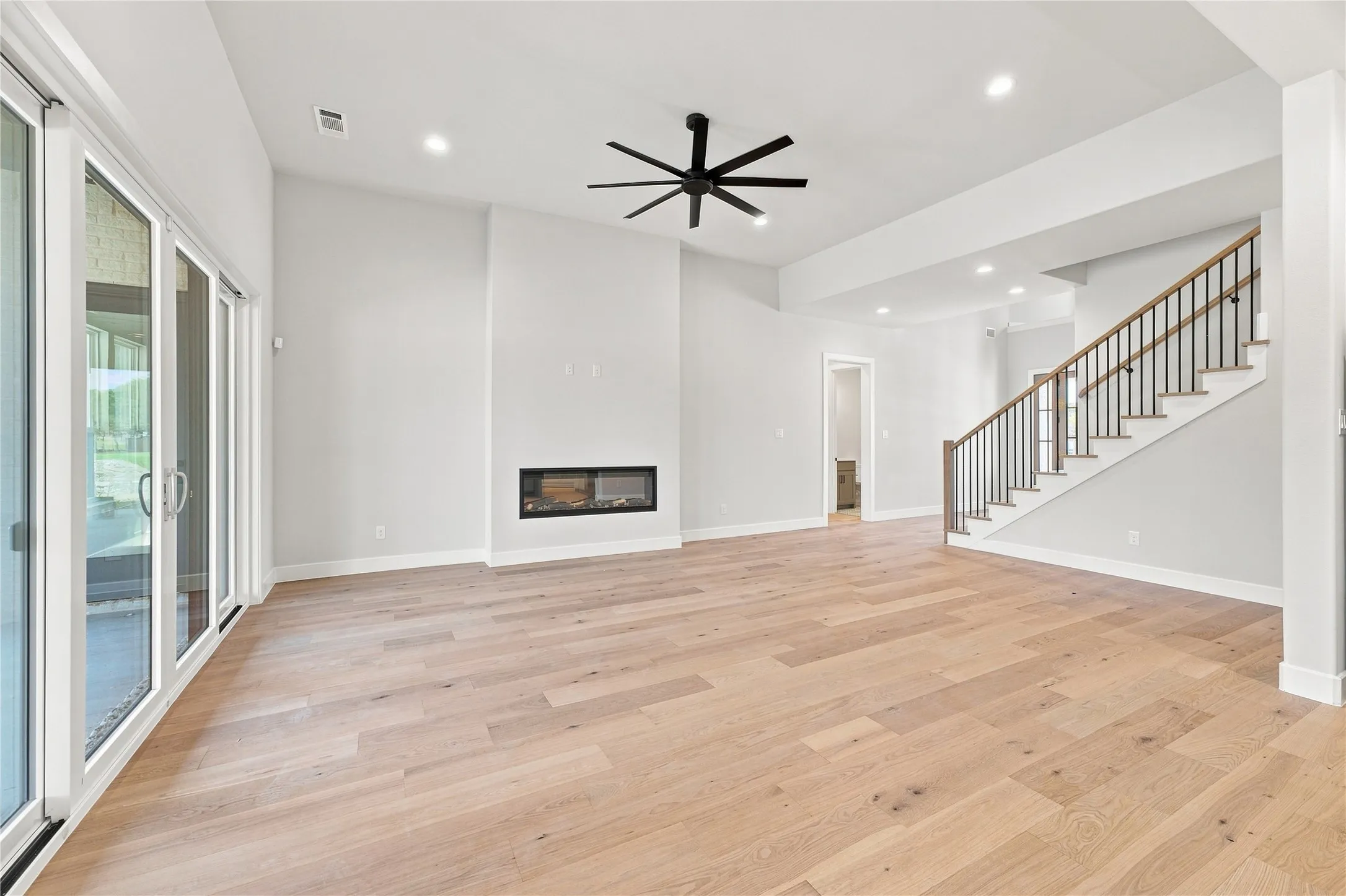 Wood-finish flooring, built-in fireplace, sliding glass doors, recessed lighting, and a staircase with wood handrails and black balusters