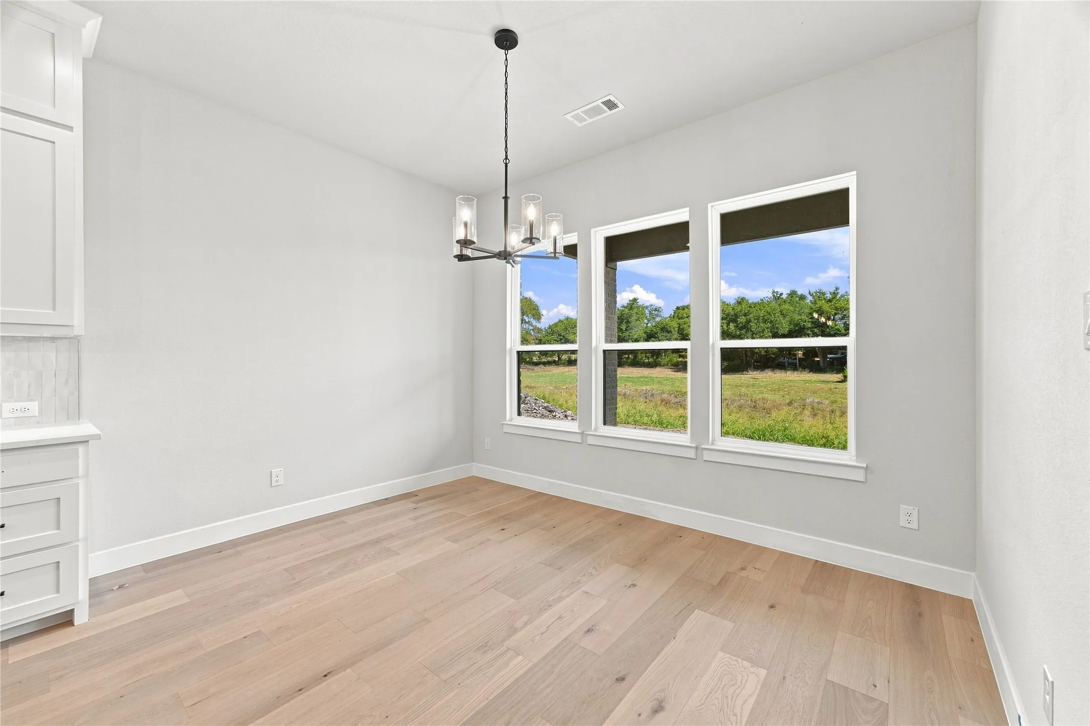 Wood-finish flooring, three large windows, a modern chandelier with clear glass shades, and white built-in cabinetry