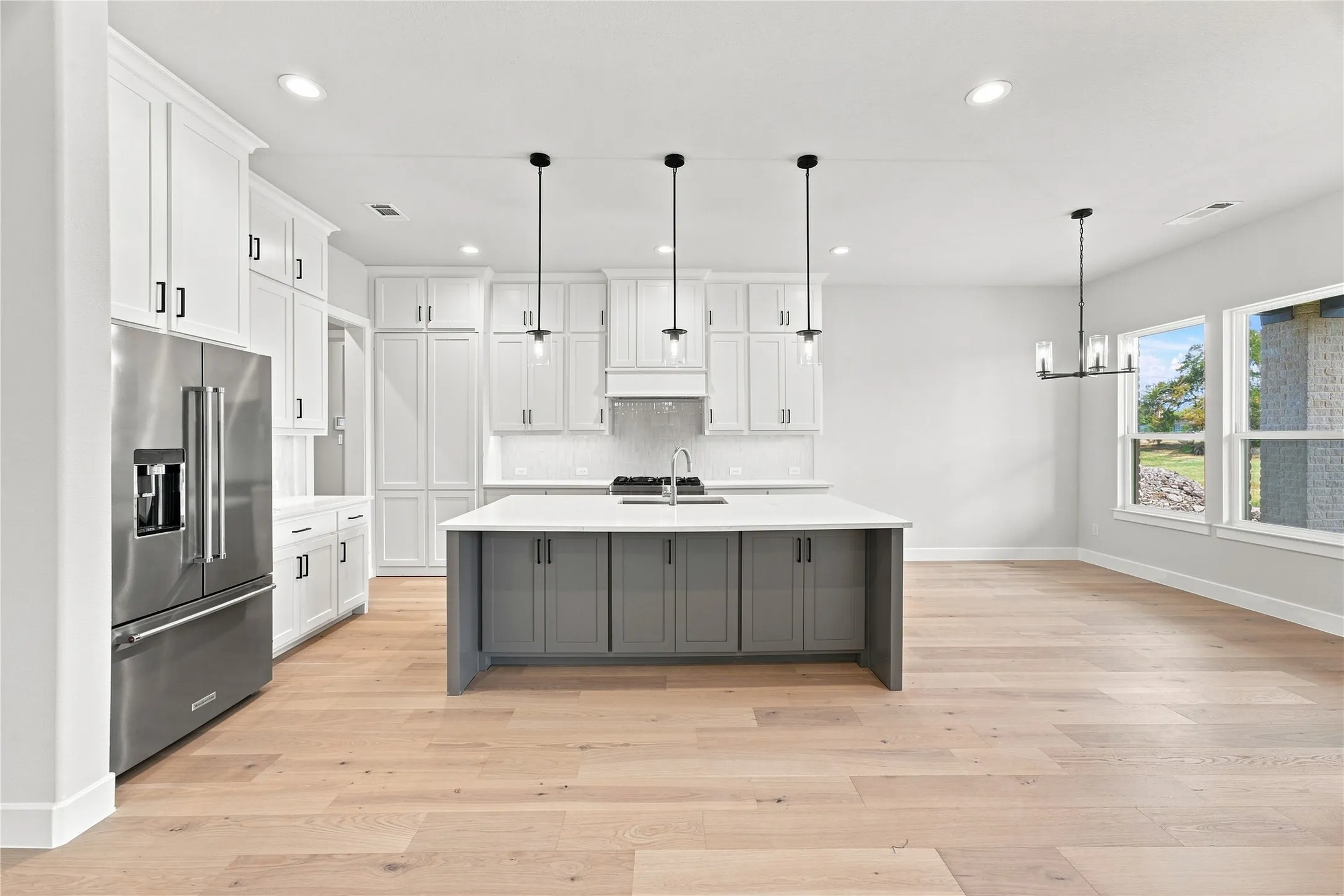 Contemporary kitchen with stainless steel appliances, light wood-finish flooring, and a gray island with a light countertop. Butler pantry door closed.