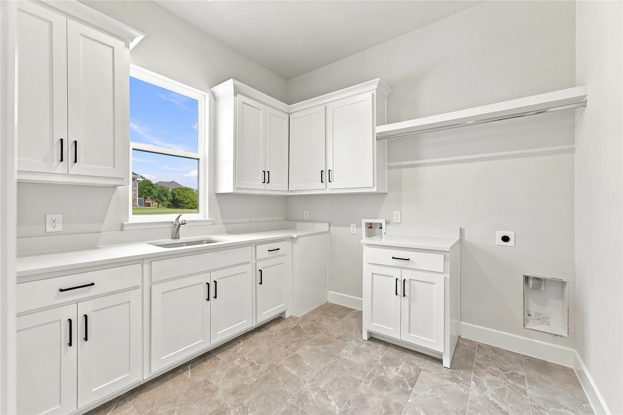White shaker-style cabinetry with black hardware, light-toned countertops, a stainless steel sink with a gooseneck faucet, a window, and a built-in hanging rod