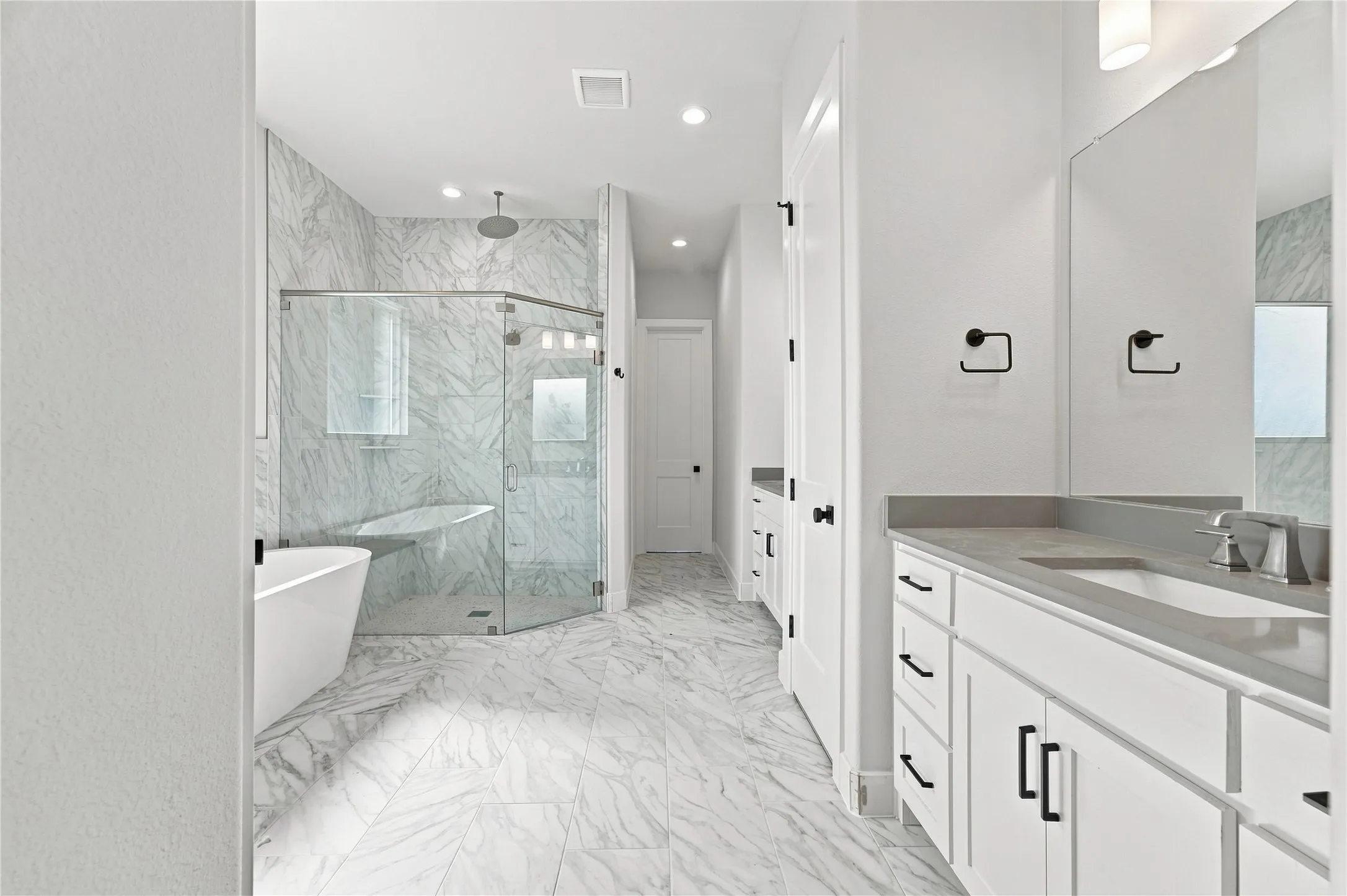 Freestanding soaking tub, frameless glass shower enclosure, dual vanity with undermount sinks, stone countertops, and marble-look tile flooring