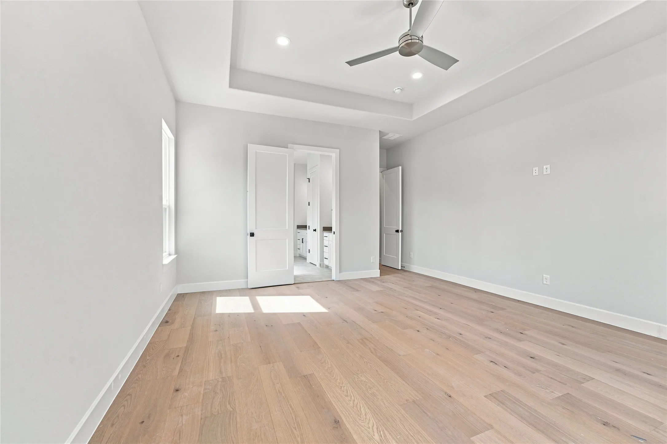 Spacious room featuring wood-finish flooring, a tray ceiling, recessed lighting, and a ceiling fan