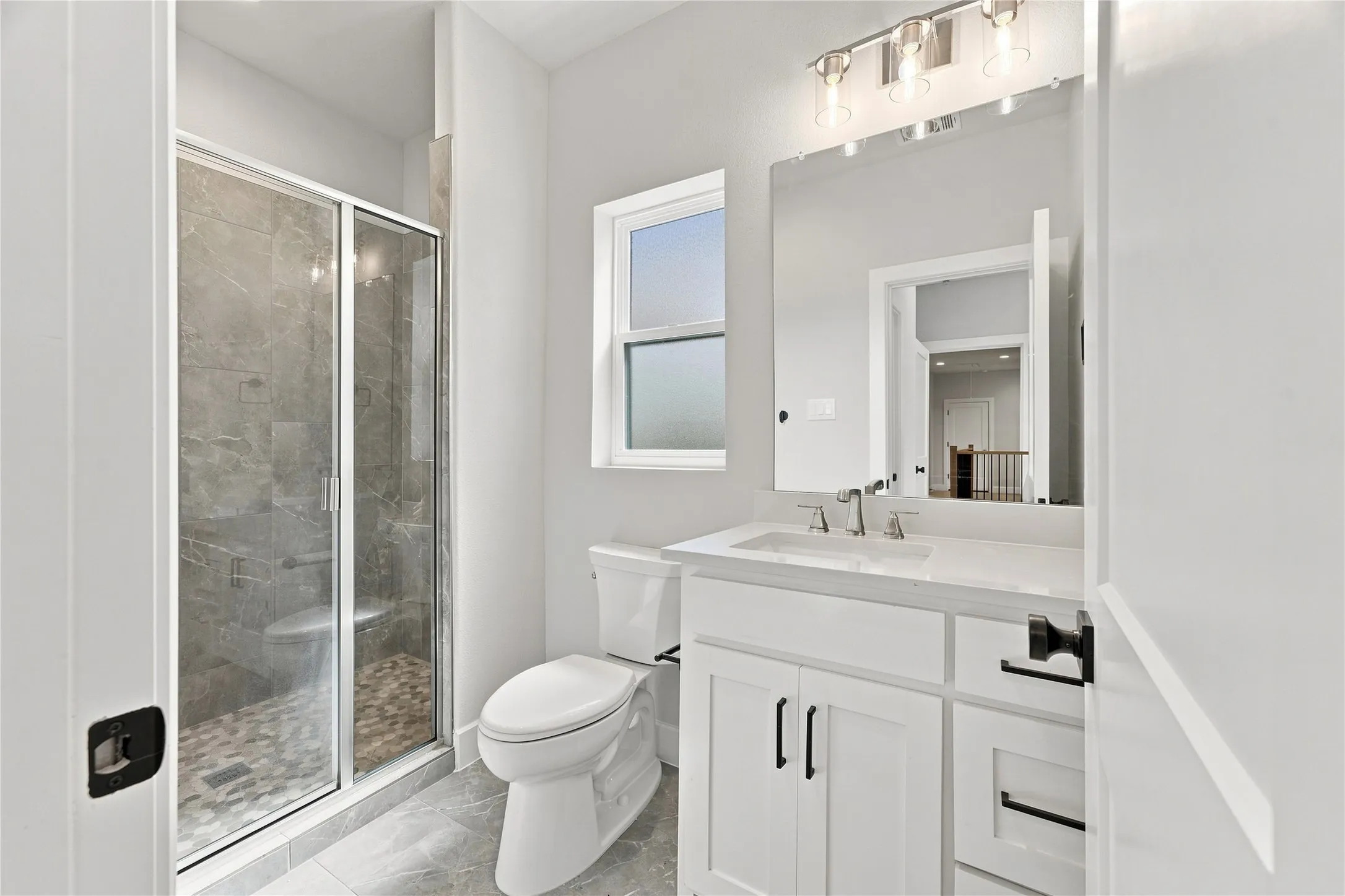 Shower with glass enclosure, white vanity with integrated sink, rectangular mirror, and window