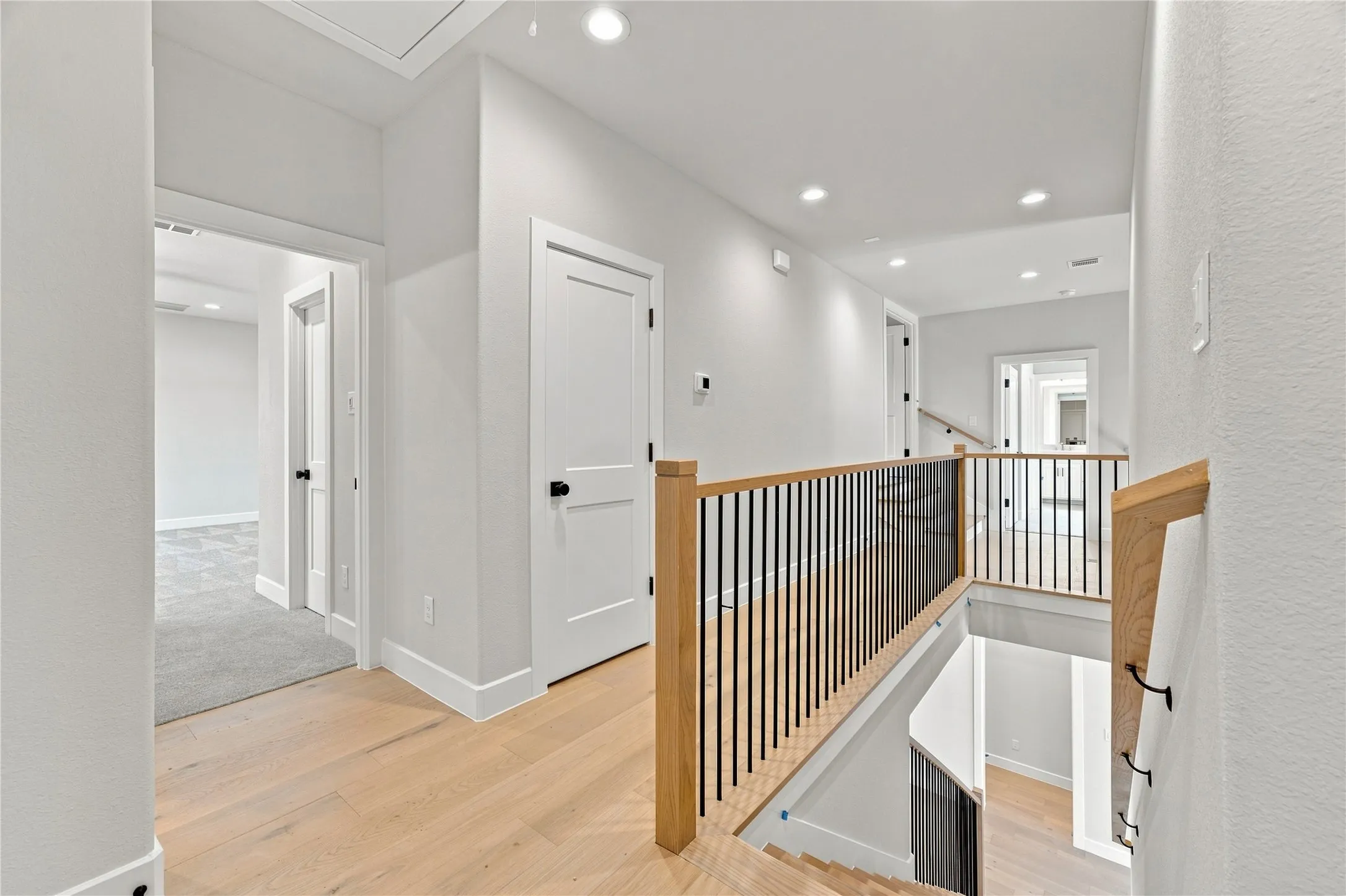 Light-toned wood-finish flooring, recessed ceiling lighting, and contemporary stair railing with wood newel posts and black balusters