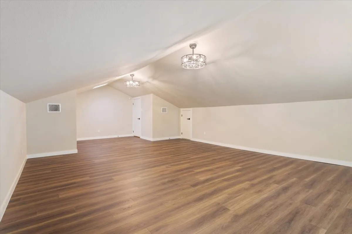 Spacious 4th bedroom / bonus room featuring LVP wood-finish flooring, a vaulted ceiling, a built-in window, two ceiling-mounted decorative light fixtures with ceiling fans (mini), and attic access