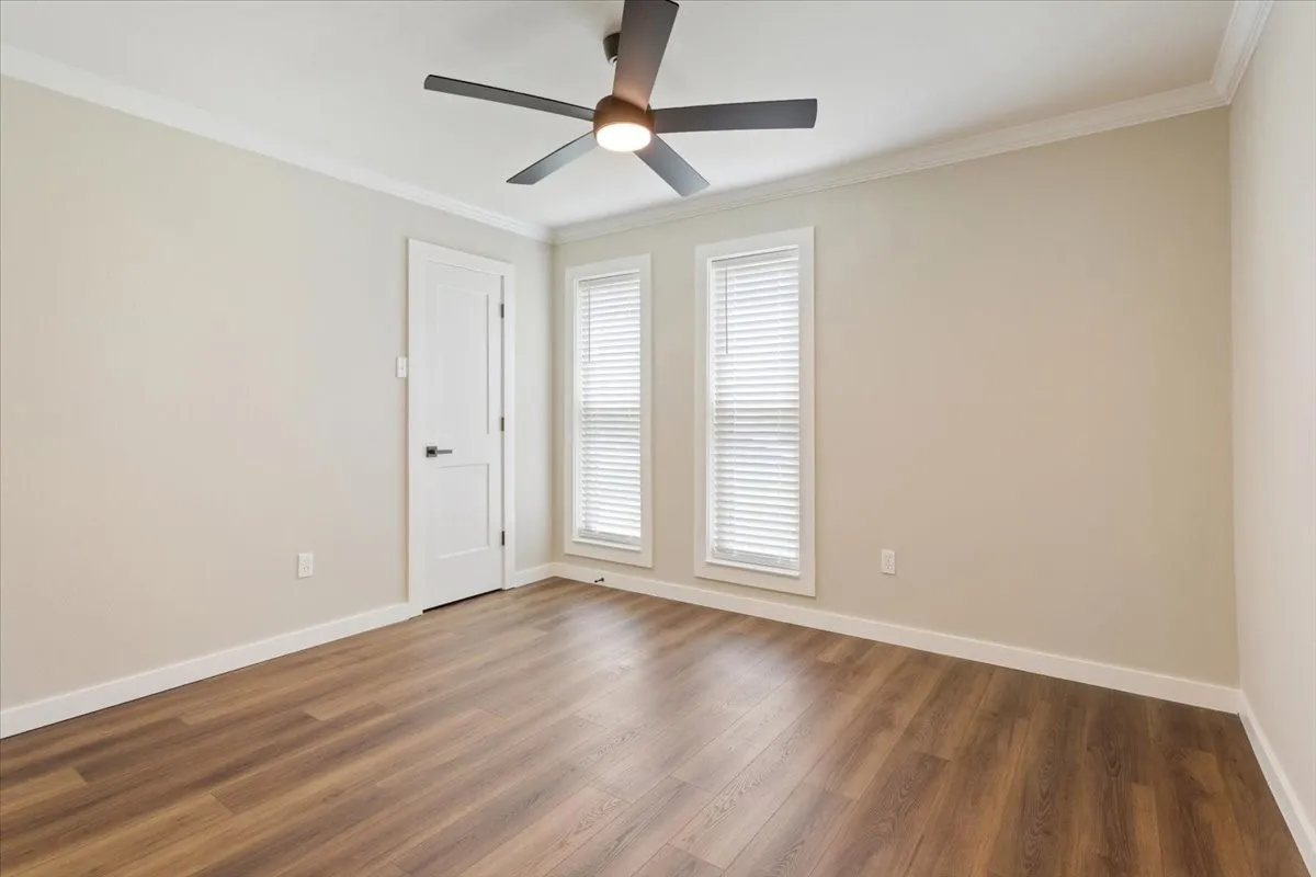 Spacious bedroom room featuring LVP wood-finish flooring, ample natural light, ceiling fan, light neutral wall paint, and white crown molding