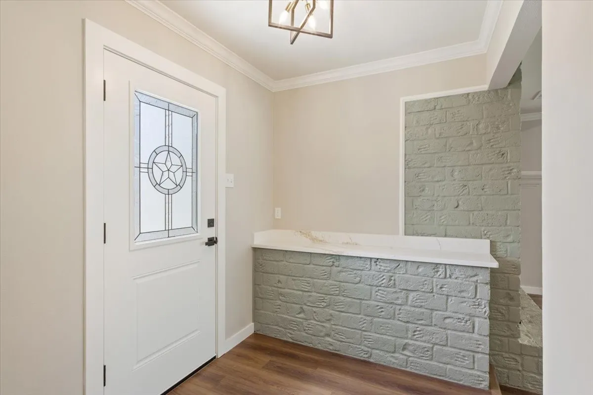 Entryway featuring a decorative glass panel front door, crown molding, wood-finish LVP flooring, and a brick-look half-wall with a light-colored quartz countertop