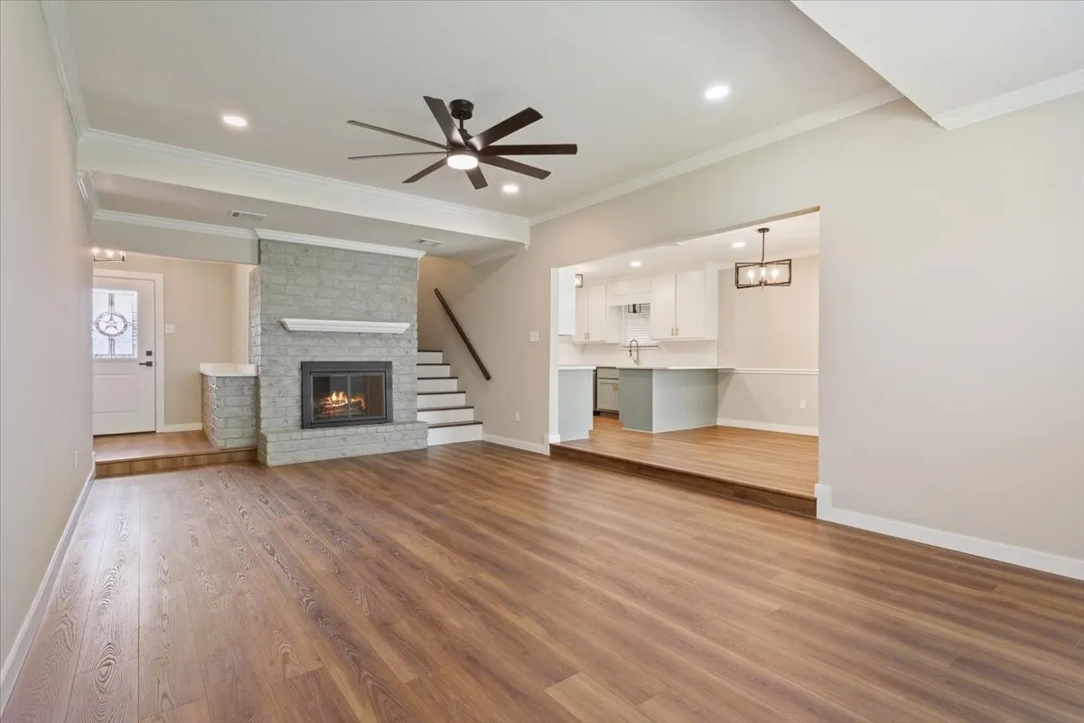 Spacious interior featuring a wood burning brick fireplace with glass doors, luxury vinyl plank wood-finish flooring, a contemporary ceiling fan, and recessed lighting