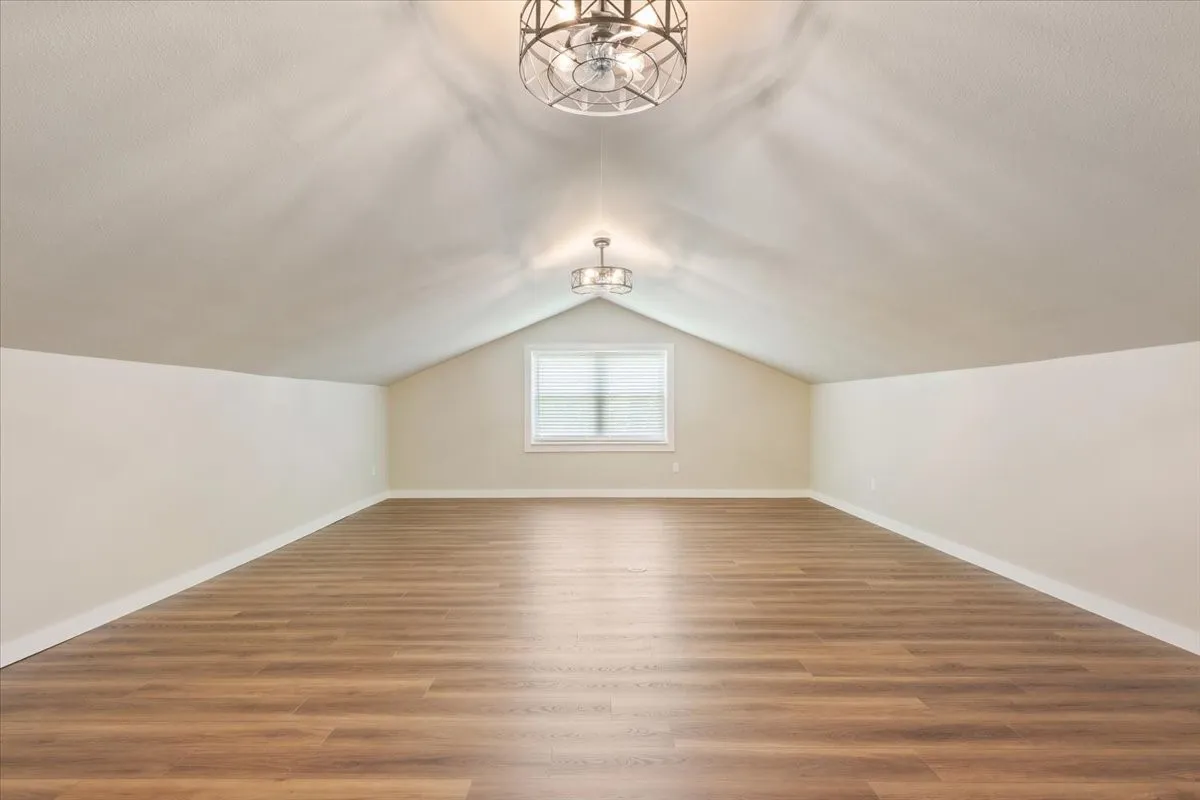Spacious 4th bedroom / bonus room featuring LVP wood-finish flooring, a vaulted ceiling, a built-in window, and two ceiling-mounted decorative light fixtures with ceiling fans (mini)