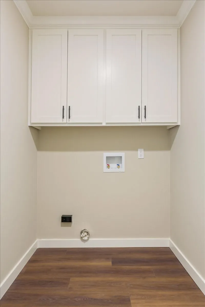 Dedicated laundry area featuring overhead white shaker-style cabinetry with matte black hardware, LVP wood-finish flooring, and white baseboards
