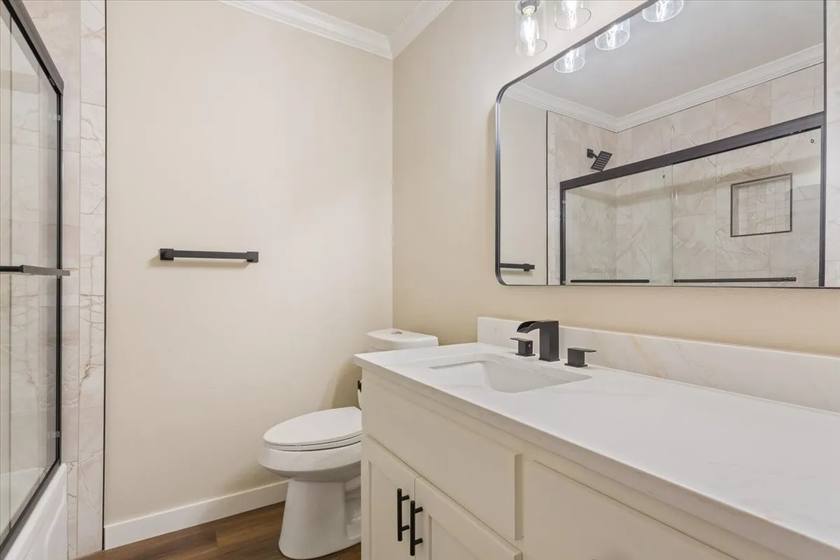 Hall bathroom with quartz countertop, undermount sink, tub/shower combo with glass door, and matte black fixtures