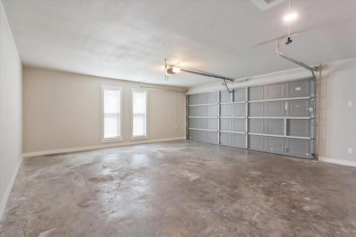 Spacious two-car garage featuring a gray sectional garage door, concrete flooring, storage closed, and two windows with blinds