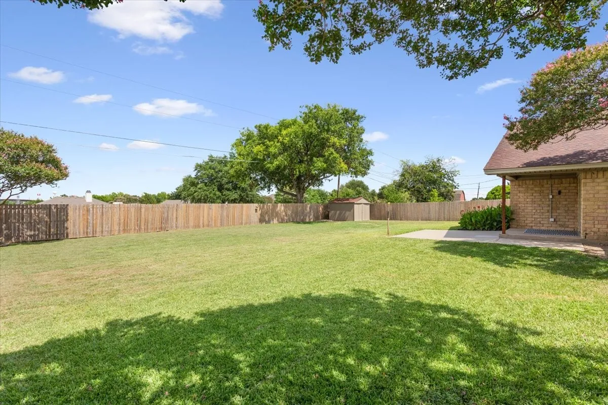Expansive backyard featuring a large grass lawn, wood privacy fencing, a concrete patio, and a storage shed