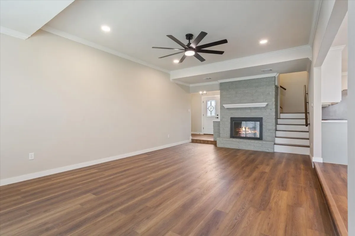 Spacious living area featuring a wood burning fireplace with glass doors, remote controlled ceiling fan, LVP wood-finish flooring, recessed lighting, and crown molding