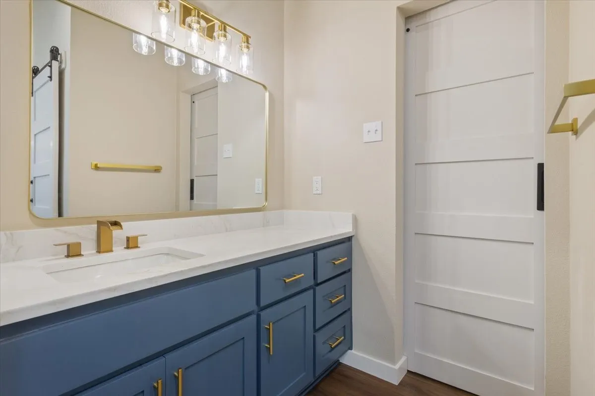 Bathroom vanity featuring a white countertop with an undermount sink, brass finish hardware, a matching brass faucet, and a large framed mirror
