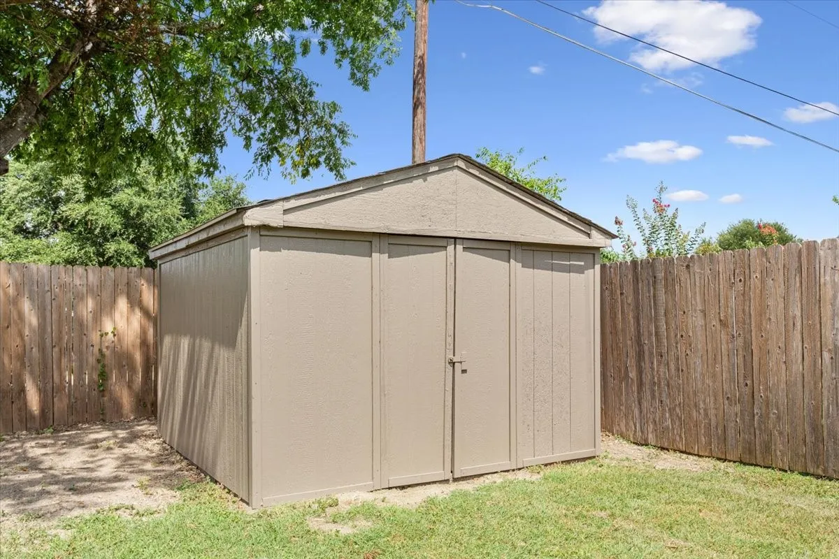 Recently painted storage shed with double doors, concrete floor, wood-paneled siding, and a surrounding wood fence