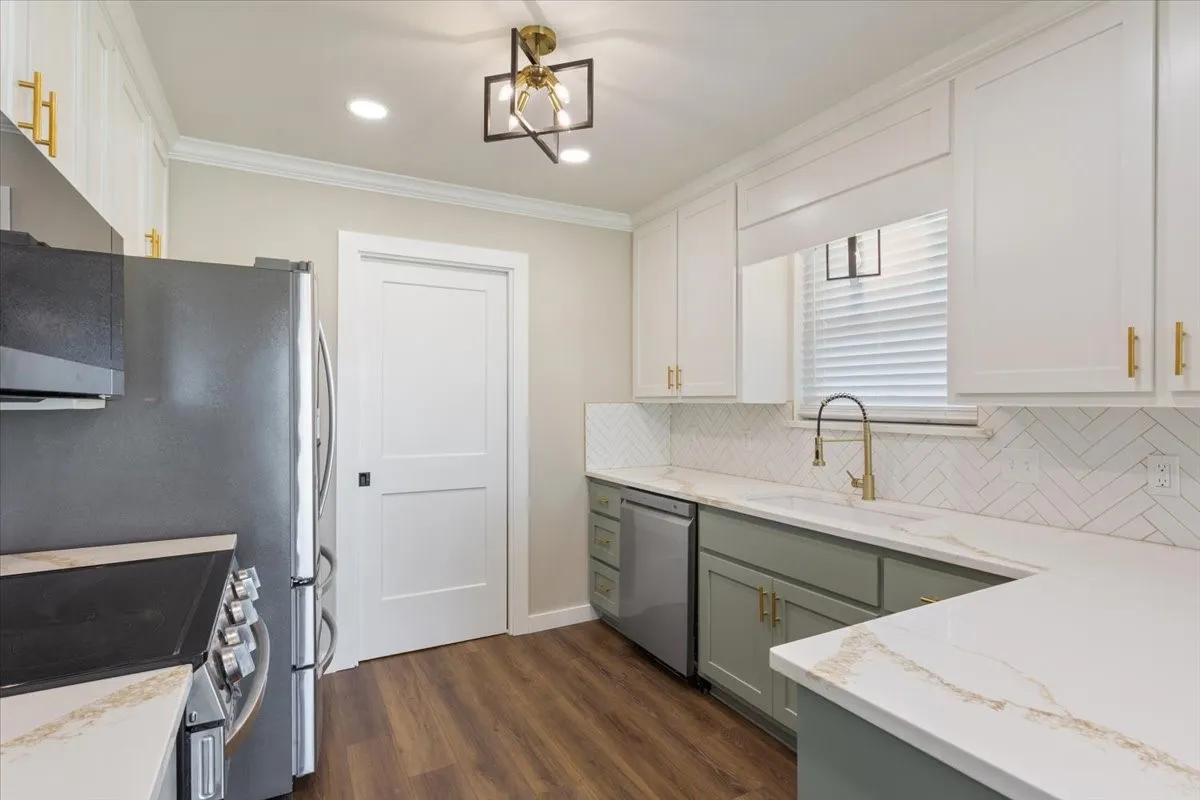 Kitchen featuring two-tone cabinetry with gold-tone hardware, white quartz countertops, stainless steel appliances, herringbone tile backsplash, and LVP wood-finish flooring