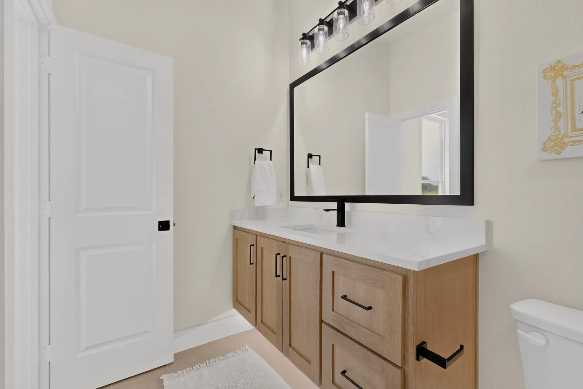 Bathroom vanity featuring light wood-finish cabinetry with black hardware, a white countertop, and an undermount sink