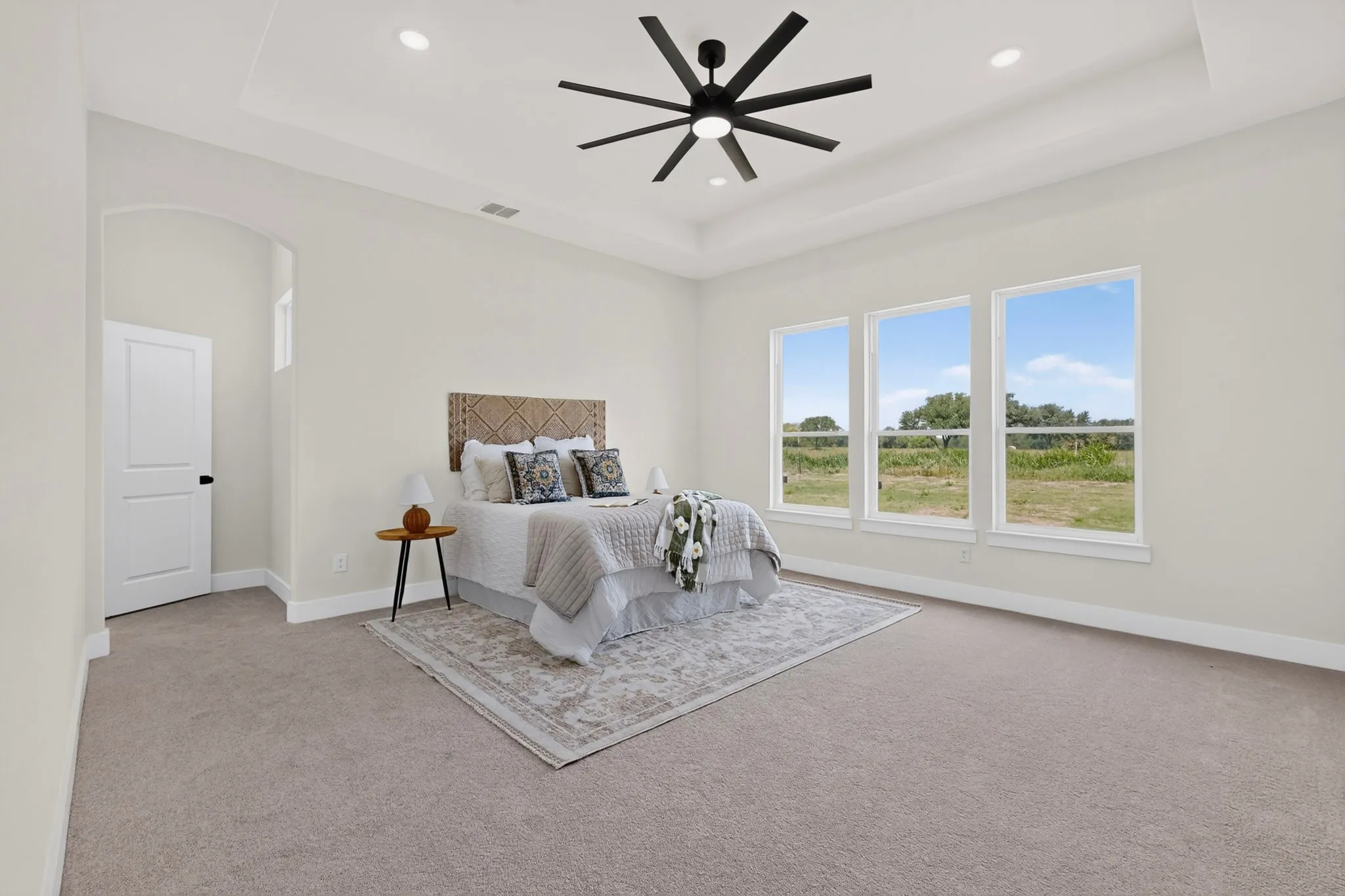 Spacious room featuring carpet flooring, a tray ceiling with recessed lighting, and a modern ceiling fan