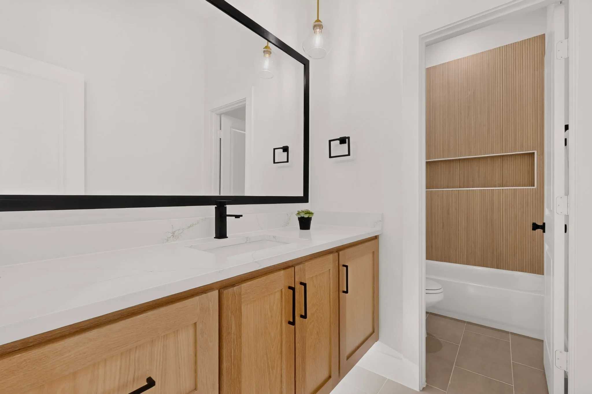 Modern vanity featuring light wood-finish cabinetry, a white countertop with integrated sink, and a matte black faucet