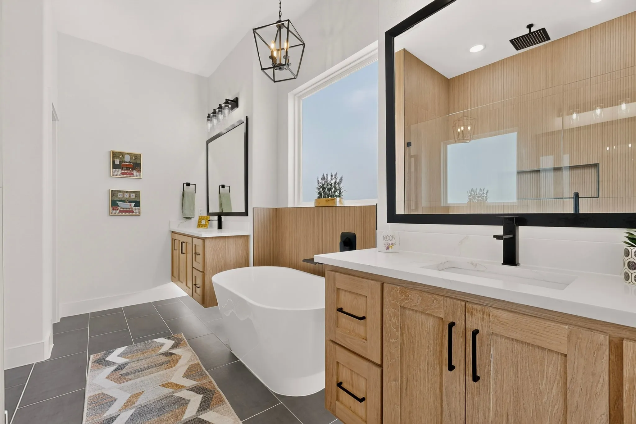 Modern bathroom featuring a freestanding soaking tub, dual vanities with light wood-finish cabinetry, and a spacious shower enclosure with a vertical slat wood-look accent wall