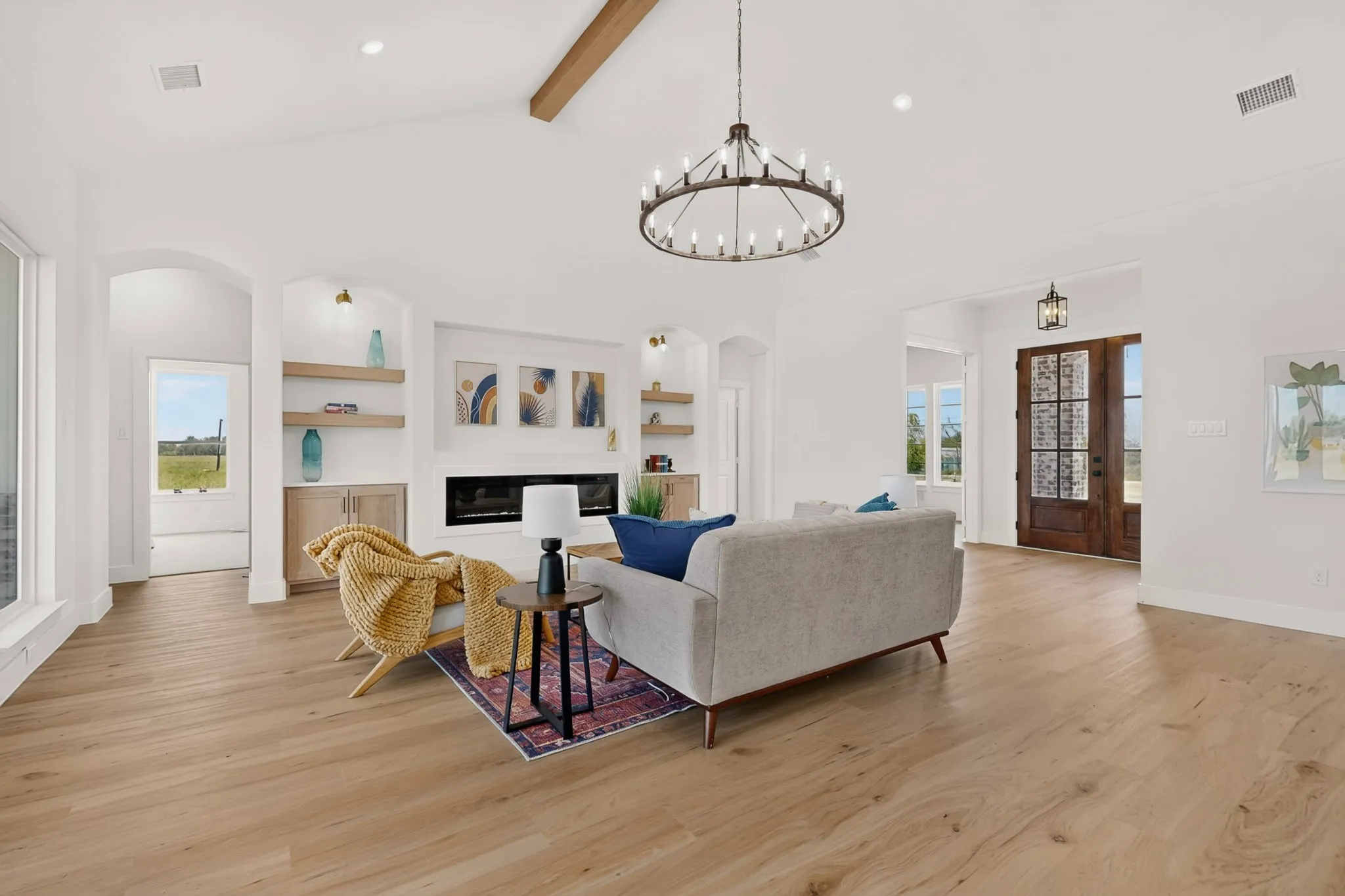 Spacious living area featuring a vaulted ceiling with exposed wood beam, a wagon wheel chandelier, and wood-finish flooring