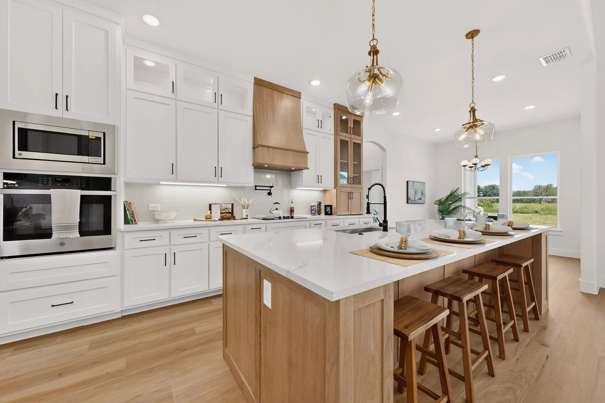 Spacious kitchen featuring an expansive central island with seating, white shaker-style cabinetry, stainless steel appliances, wood-finish flooring, and pendant lighting fixtures