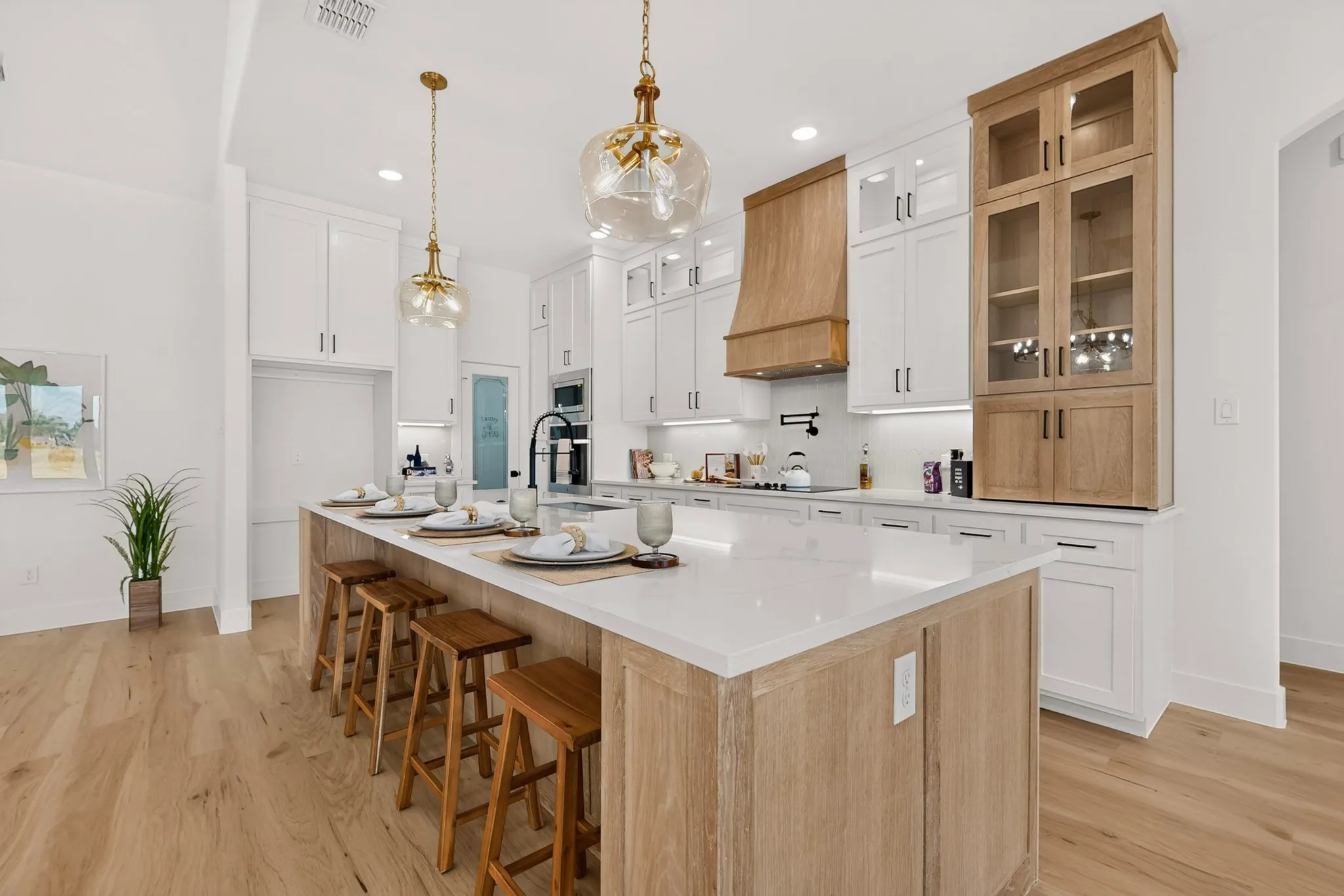 Spacious kitchen featuring a large central island with seating, light wood-finish flooring, white cabinetry with contrasting wood-finish accents, and recessed and pendant lighting fixtures