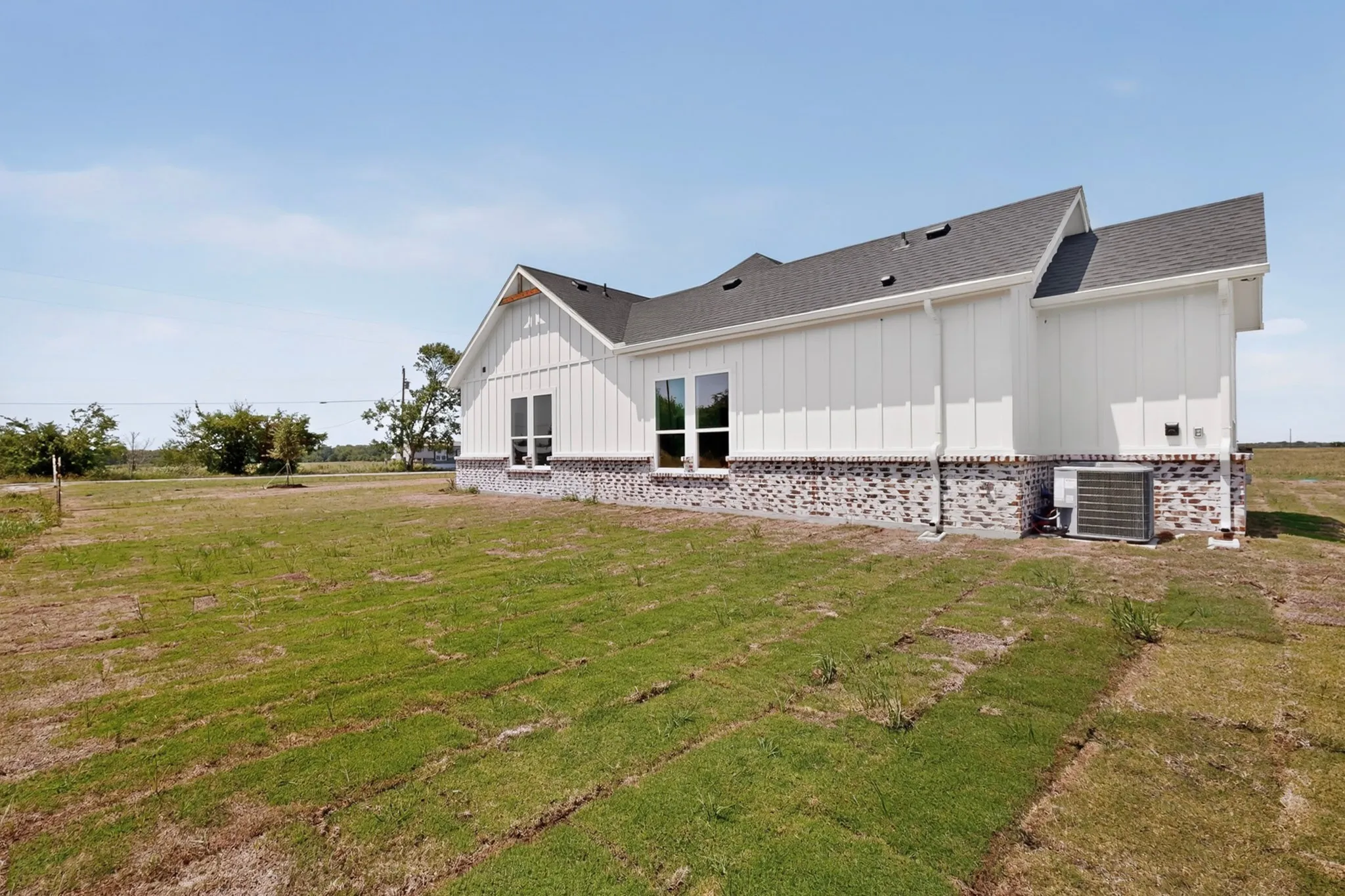 Spacious lot featuring a newly constructed residence with board and batten siding, dark brick skirting, and a dark shingle roof
