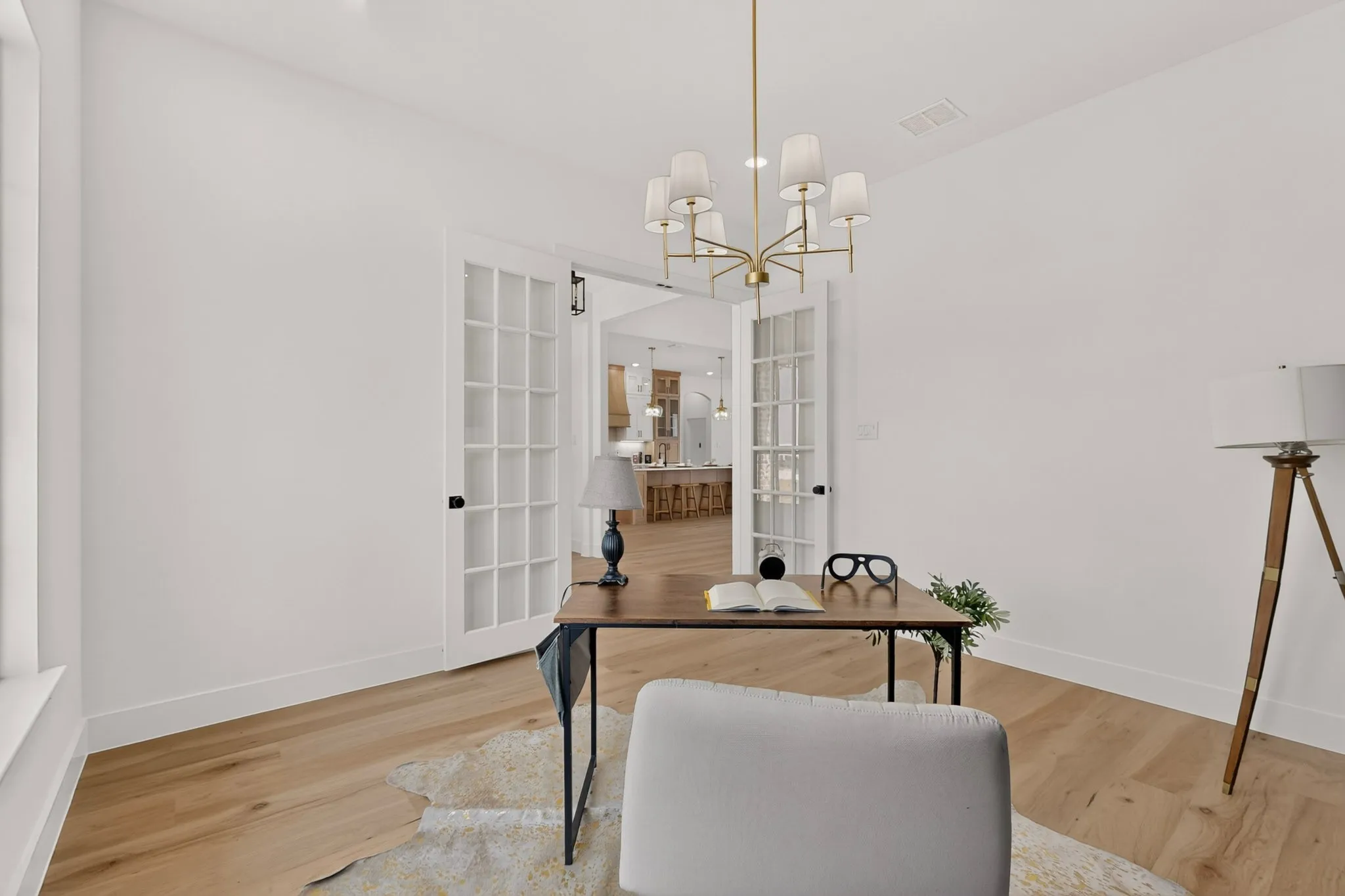 Bright room featuring light wood-finish flooring, white walls, and a contemporary brass chandelier