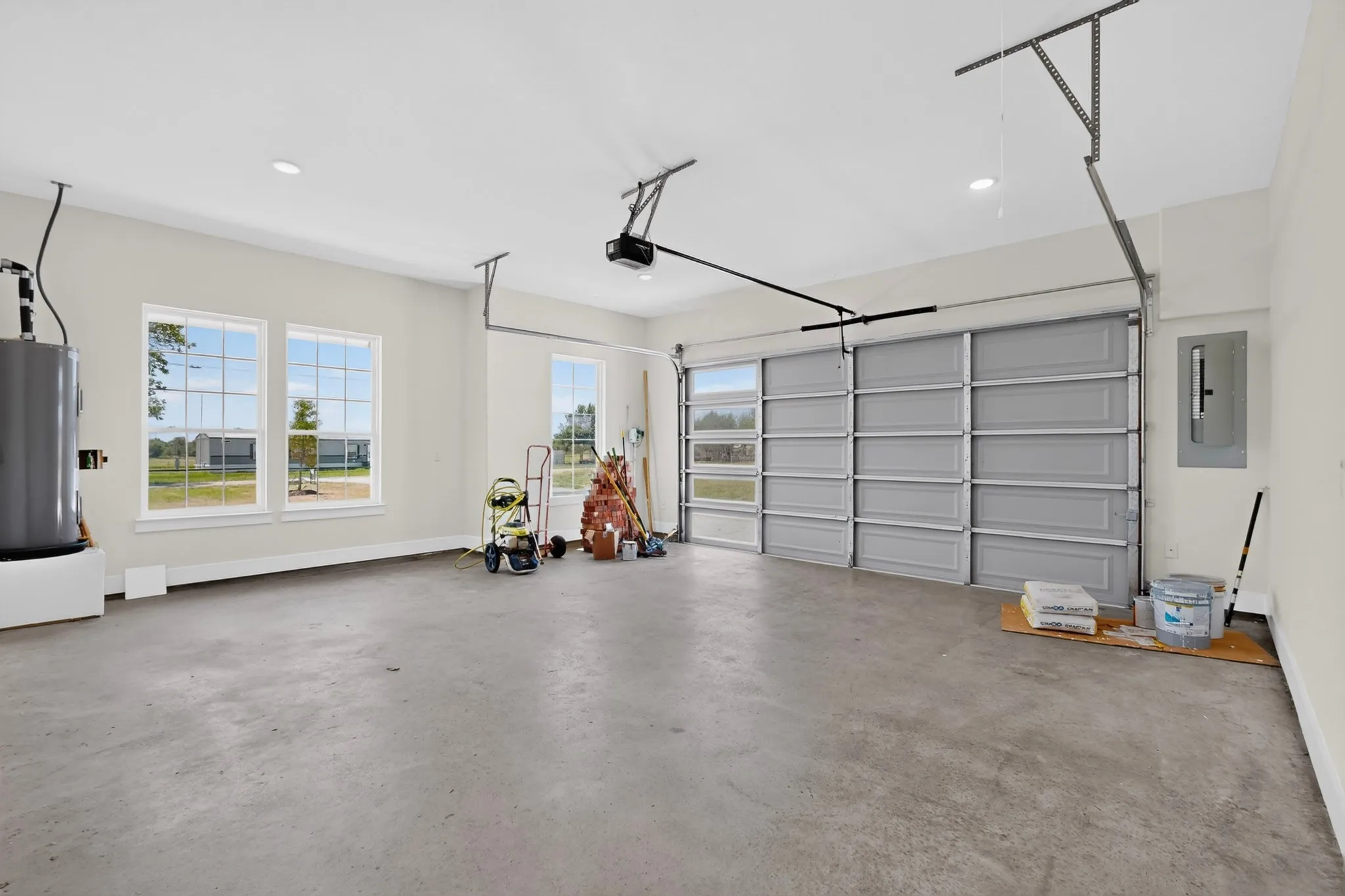 Spacious garage featuring a concrete floor, multiple windows providing natural light, a sectional garage door with upper window panels, and a ceiling-mounted garage door opener