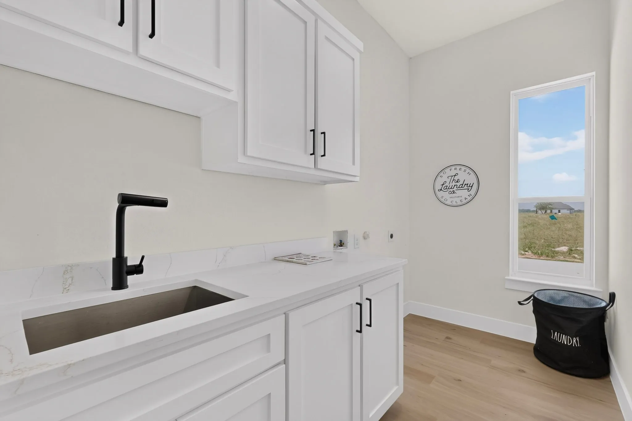 Laundry room featuring white cabinetry, a rectangular undermount sink with a matte black faucet, white countertops, and wood-finish flooring