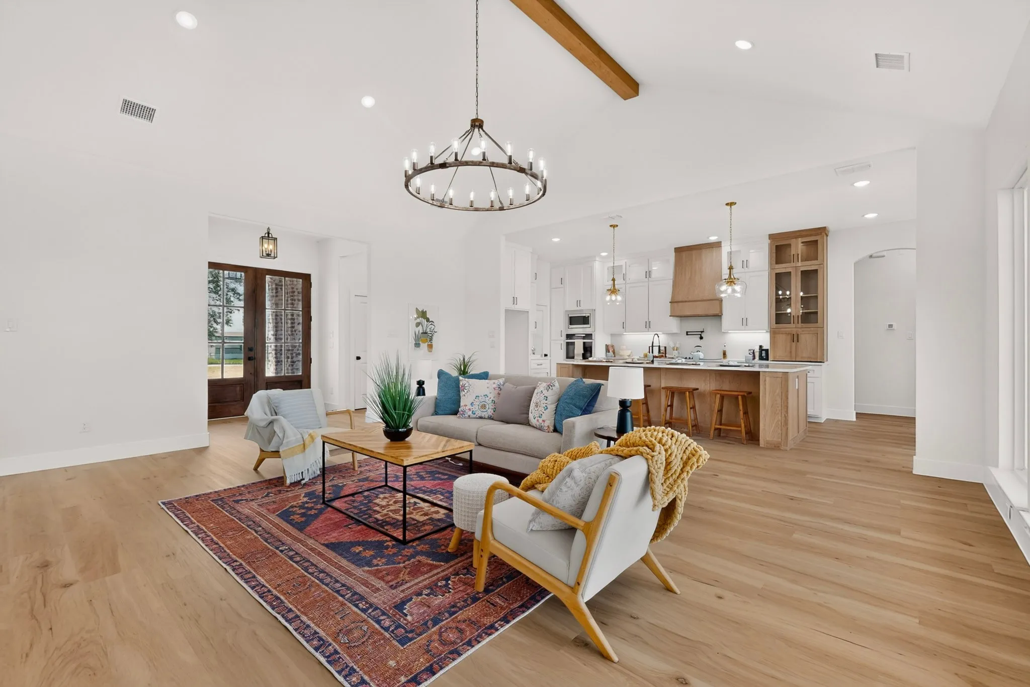 Spacious open-concept living area featuring wood-finish flooring, a vaulted ceiling with an exposed wood beam, and a wagon wheel chandelier
